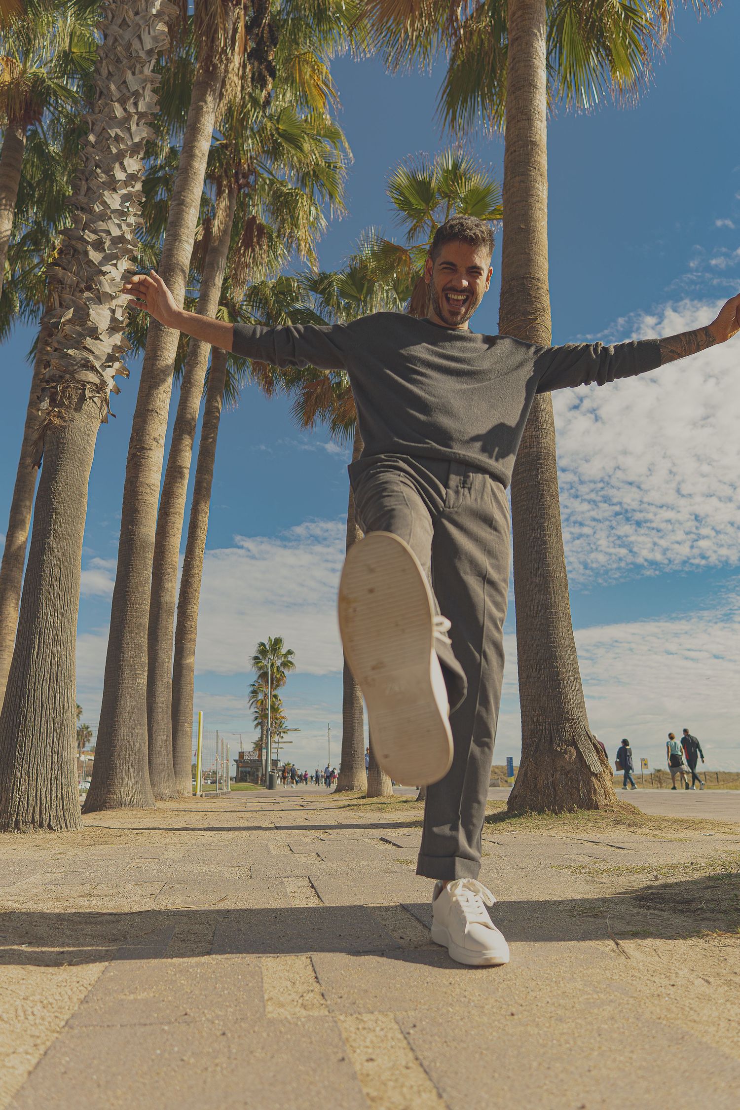 Man balancing on skateboard along palm tree-lined path at Venice Beach on a sunny day.