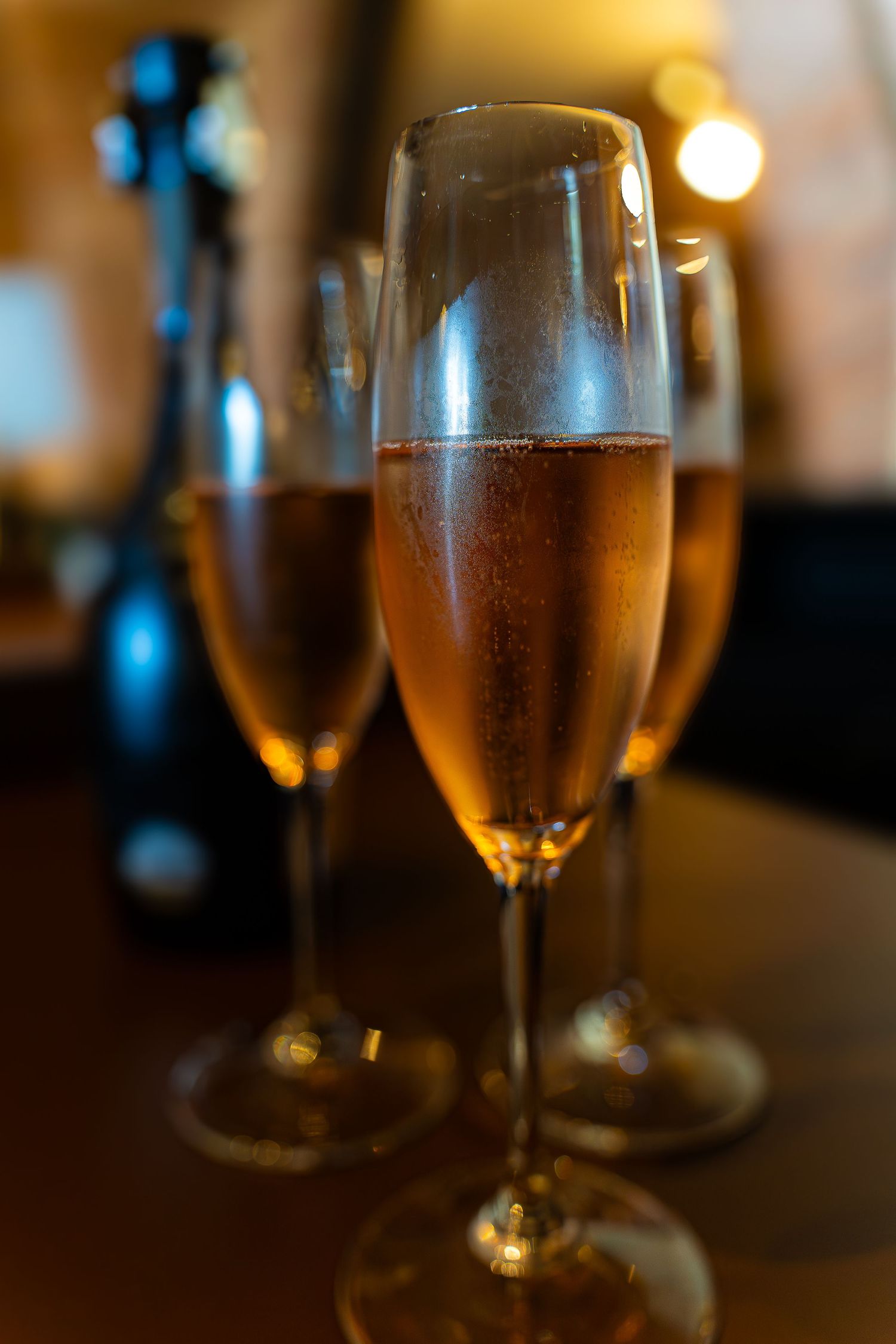 Primer plano de cava dorado rosado en copas de cava sobre una mesa de madera oscura con una cálida iluminación ambiental.