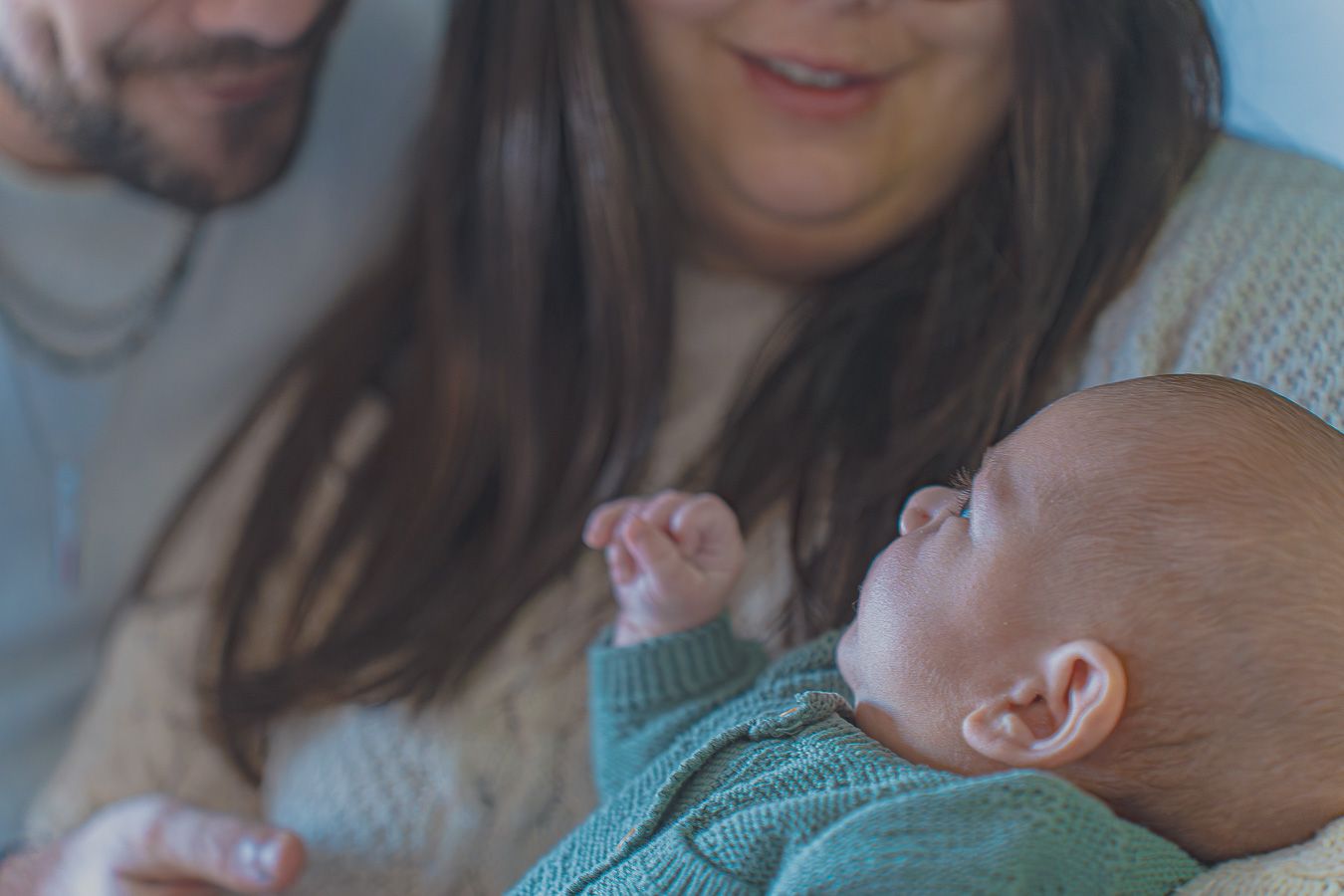 New parents smiling and holding their sleeping newborn baby dressed in a green knit outfit.