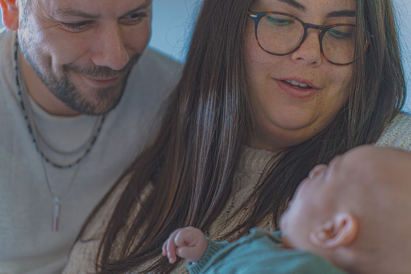 Padres sonriendo mientras miran con ternura a su bebé, fotografía de maternidad y familia en casa en Barcelona, Meraki by VGracia