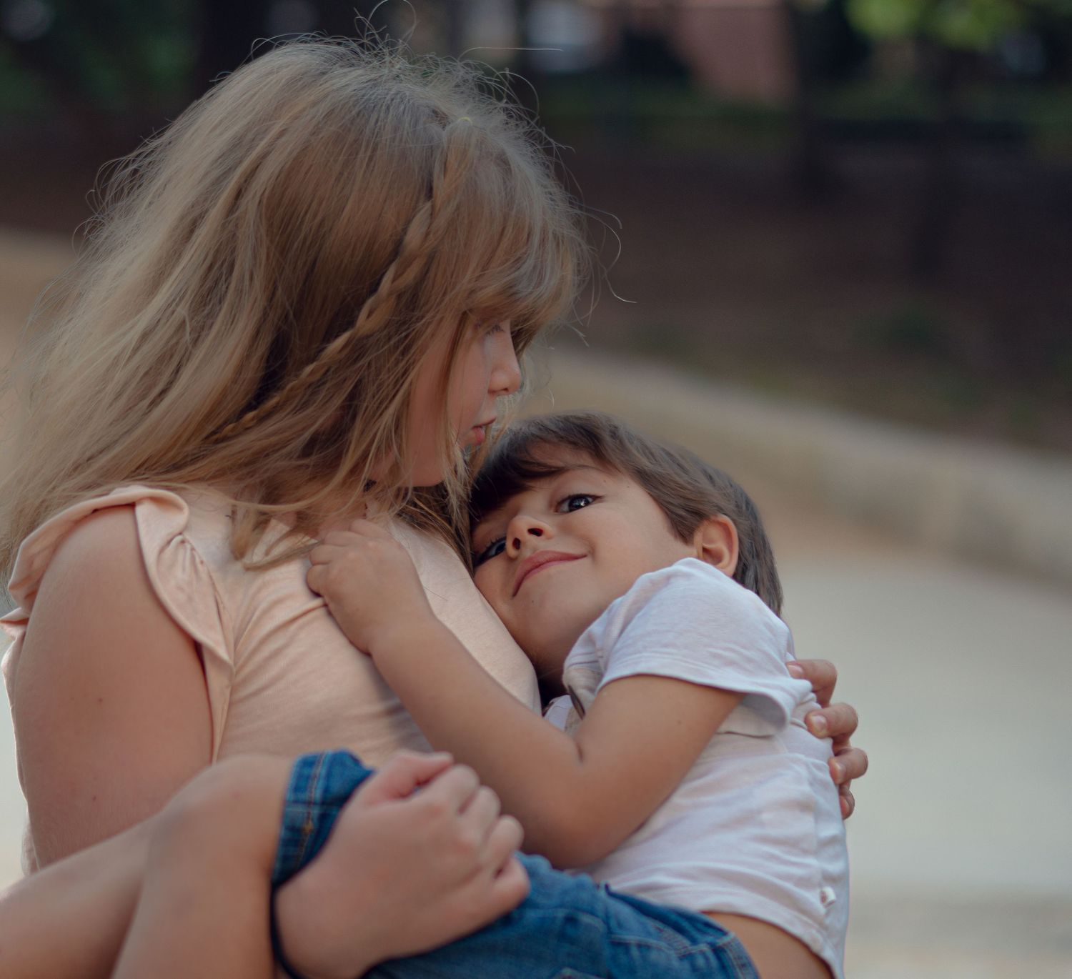 Two young girls sharing a tender hug outdoors, with the older girl gently embracing the younger child.