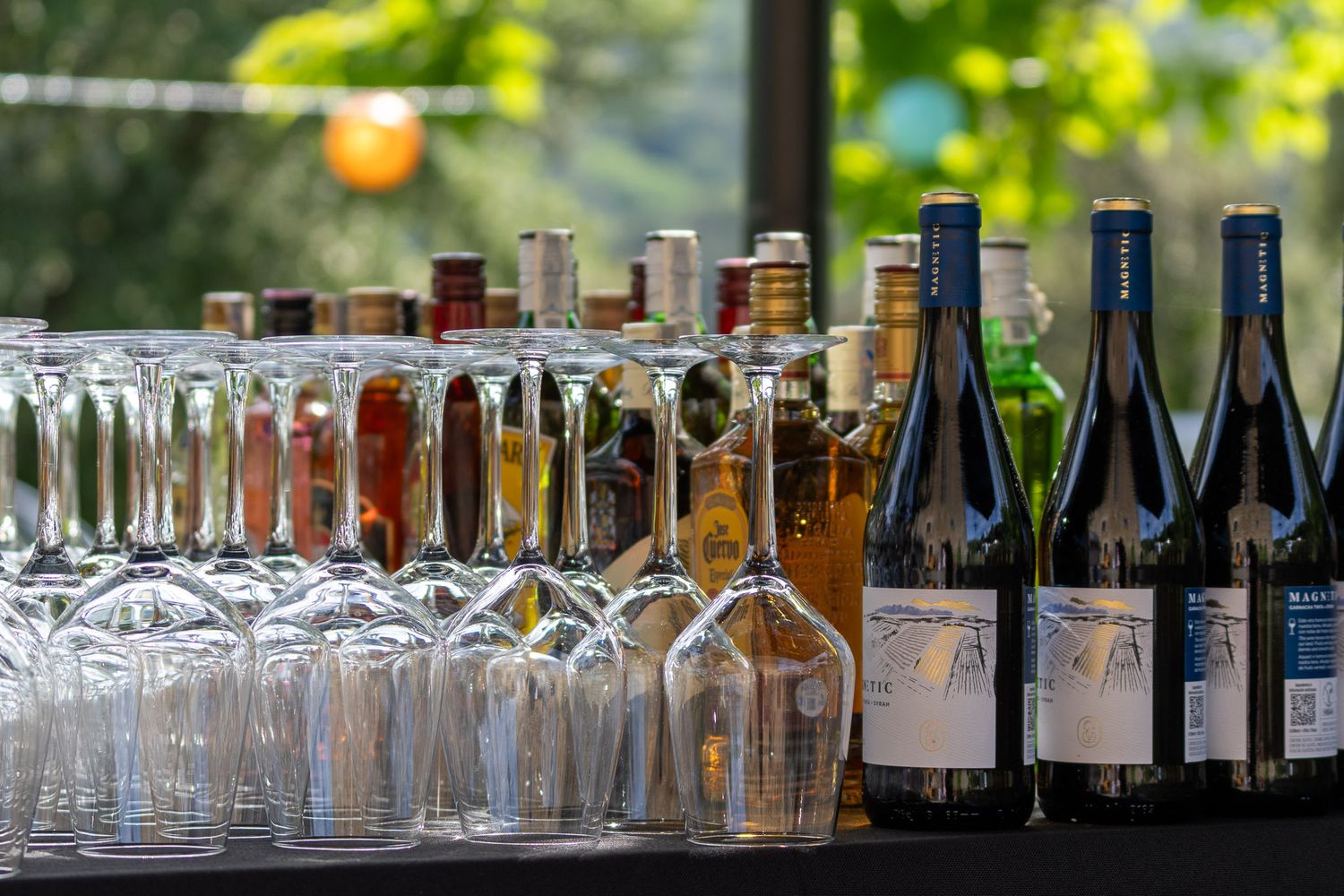 Close-up of assorted wine and liquor bottles lined up with elegant wine glasses at an outdoor bar display.