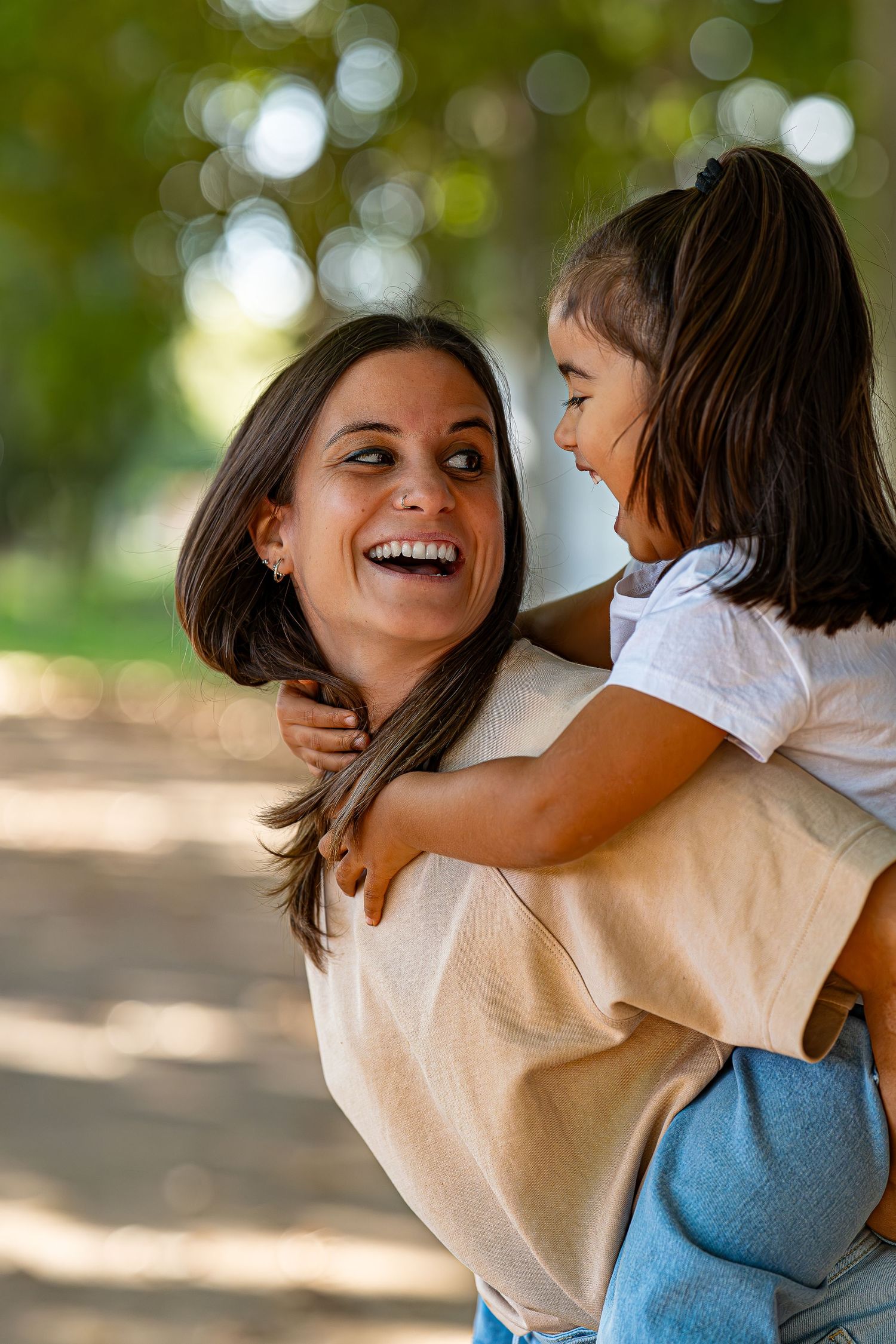 Una madre y su hija felices comparten un tierno momento al aire libre con una iluminación bokeh natural al fondo.