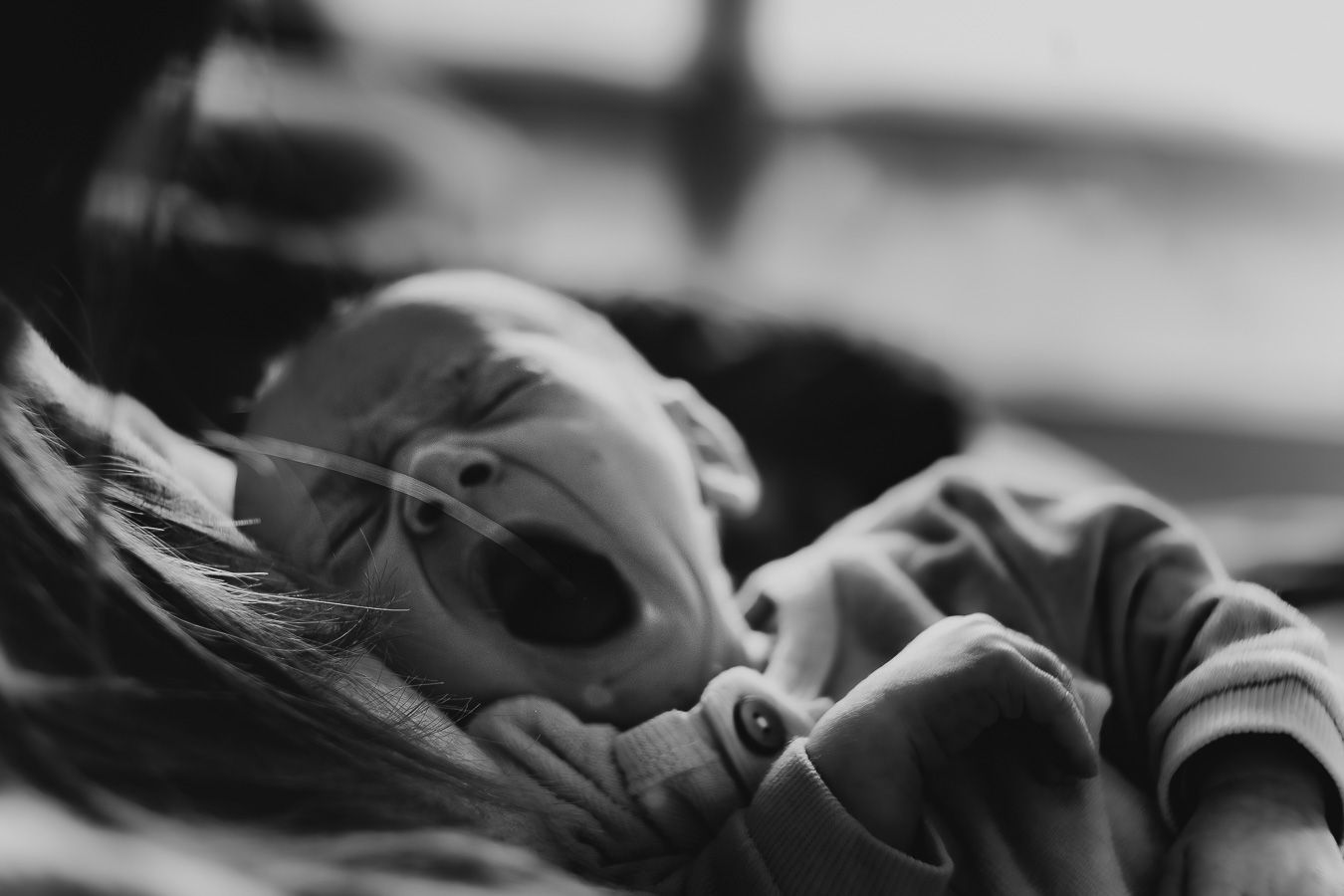 Black and white photo of a newborn baby yawning while being cradled in a parent's arms.