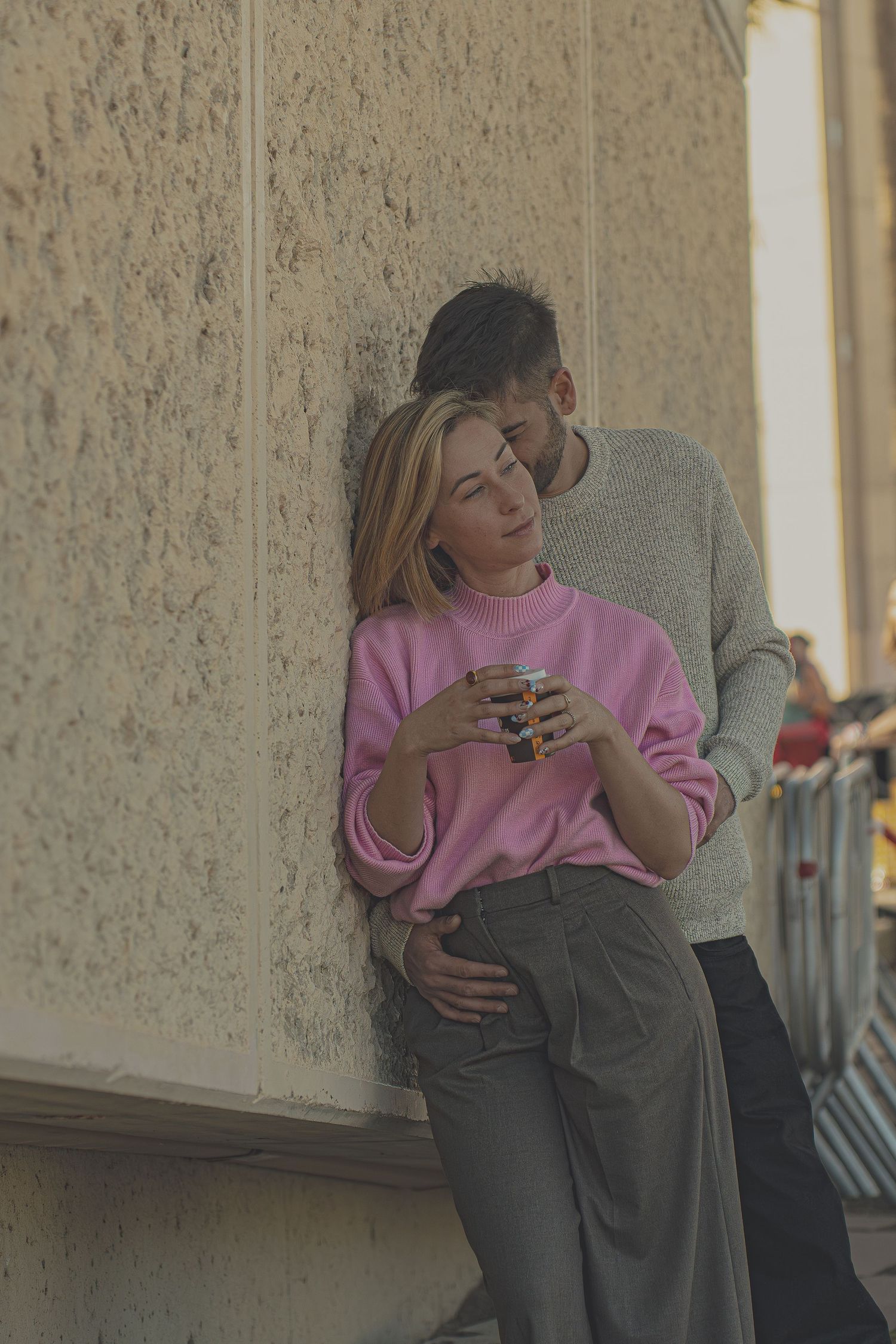 Pareja joven abrazándose de forma romántica y casual contra una pared texturizada, sesión de fotos de pareja urbana en Barcelona, Meraki