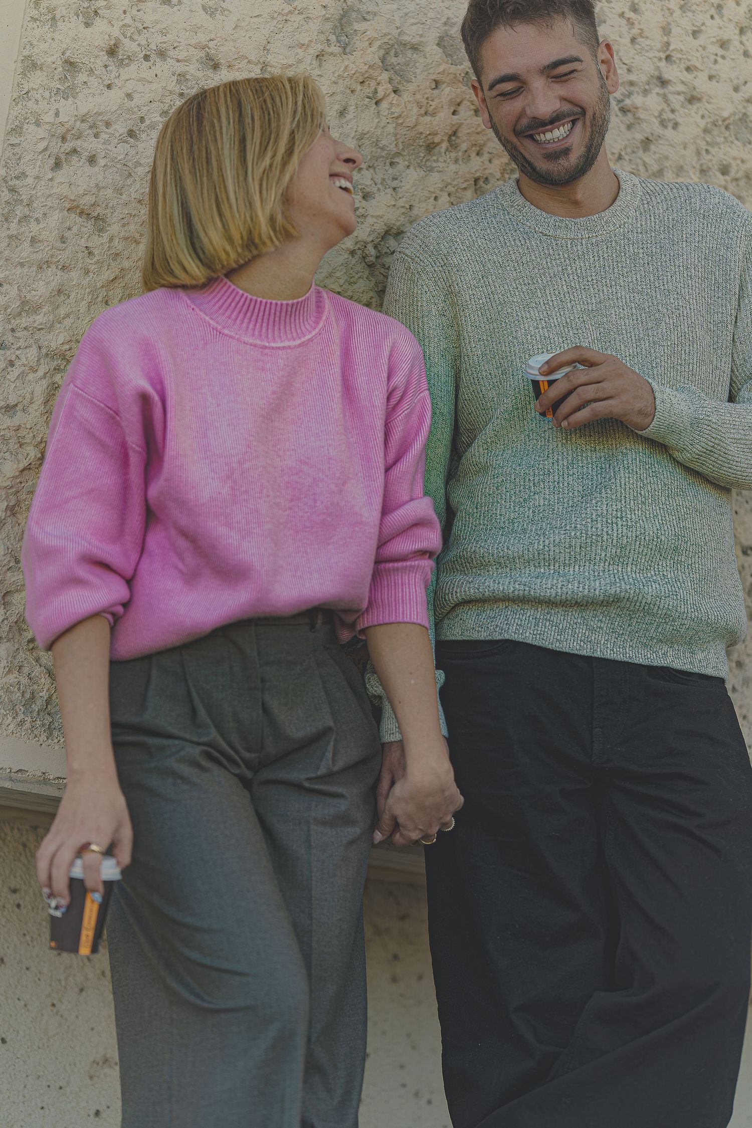 Pareja riendo y mirándose con complicidad apoyados en una pared, sesión de fotos de pareja urbana y natural en Barcelona, Meraki by VGracia.