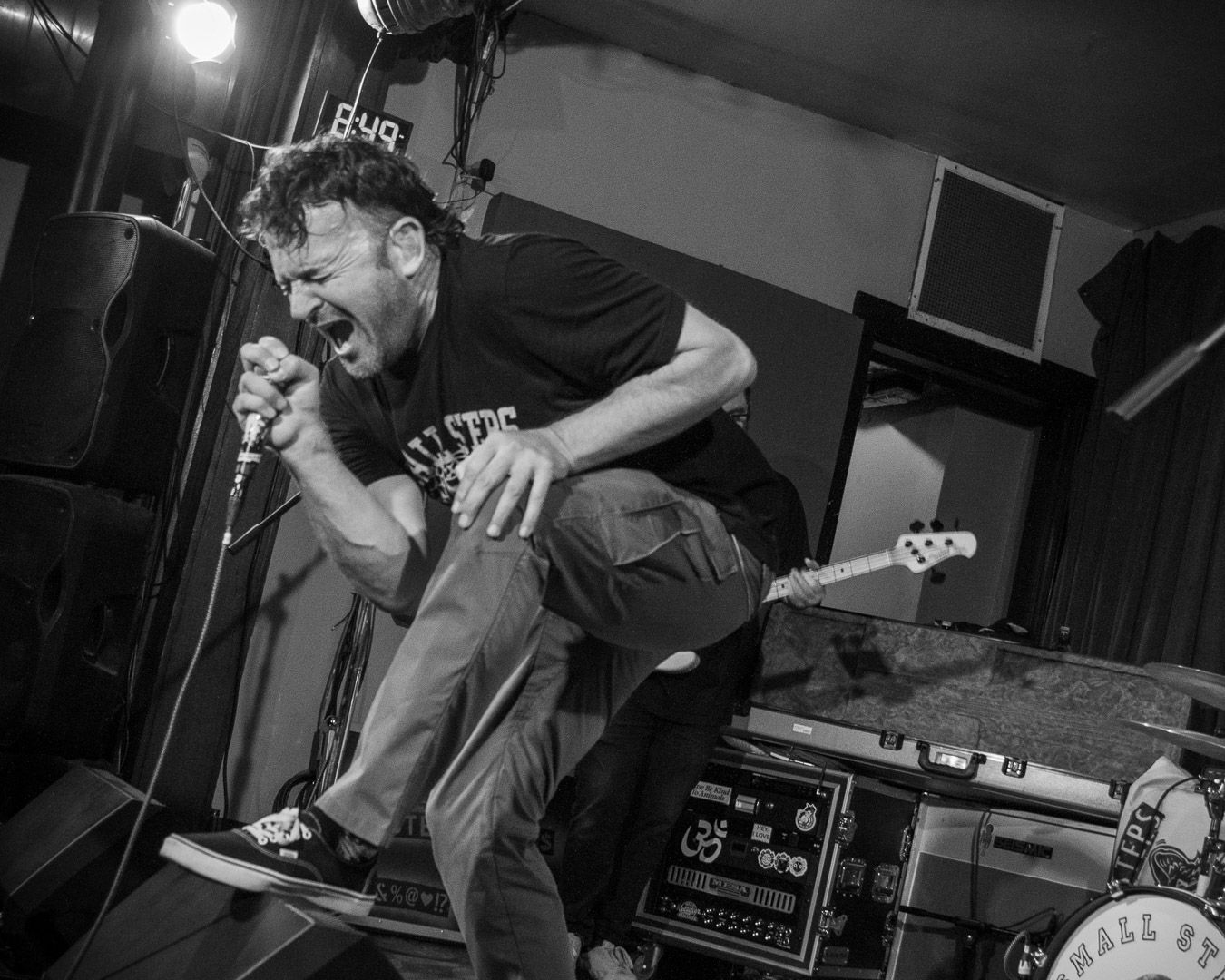Black and white photo of punk rock singer performing passionately on stage, captured mid-shout during an energetic live show.