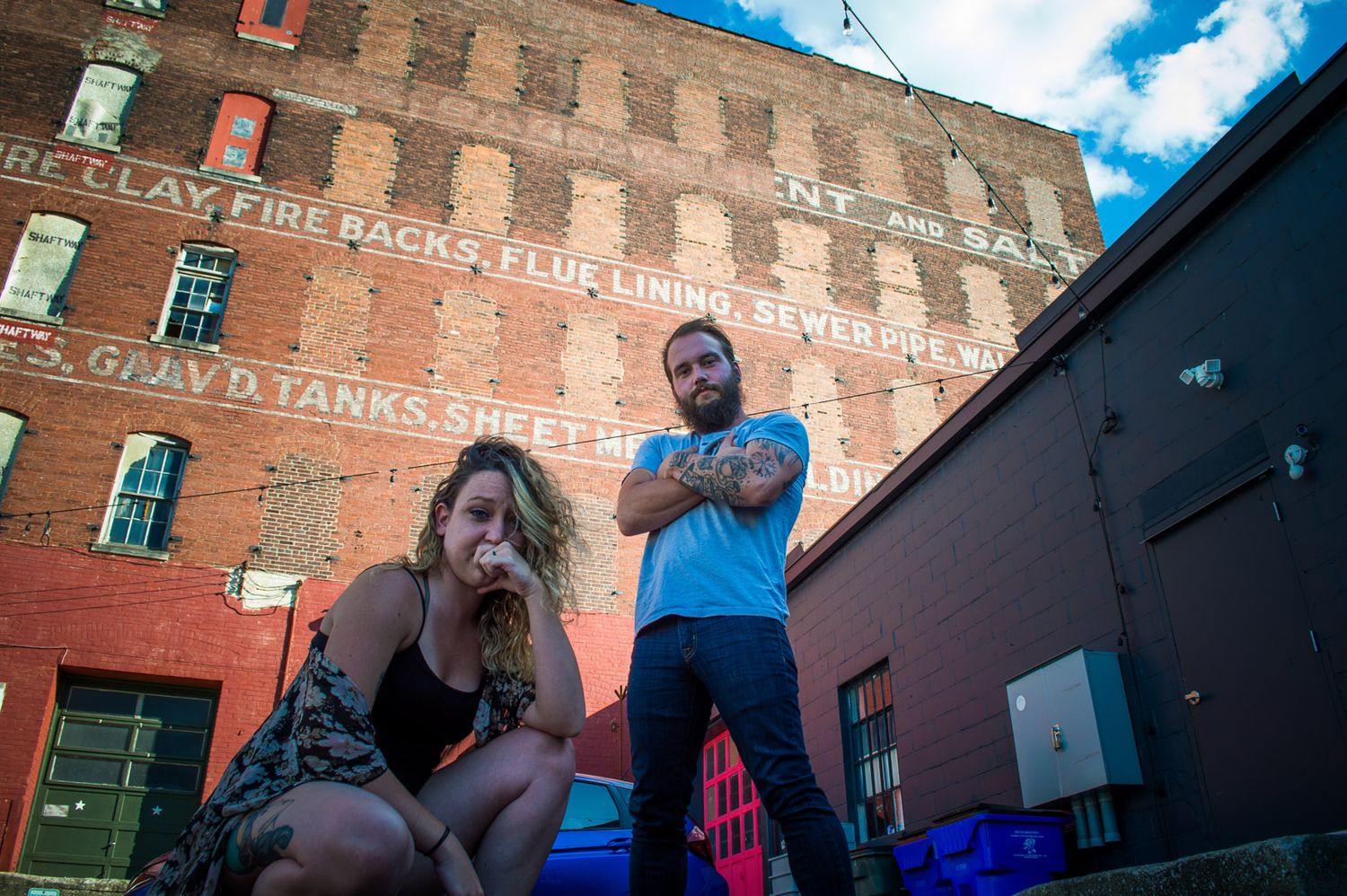 Urban portrait of two people posing in front of a brick building in downtown Kentucky under blue sky, creative lifestyle photography.
