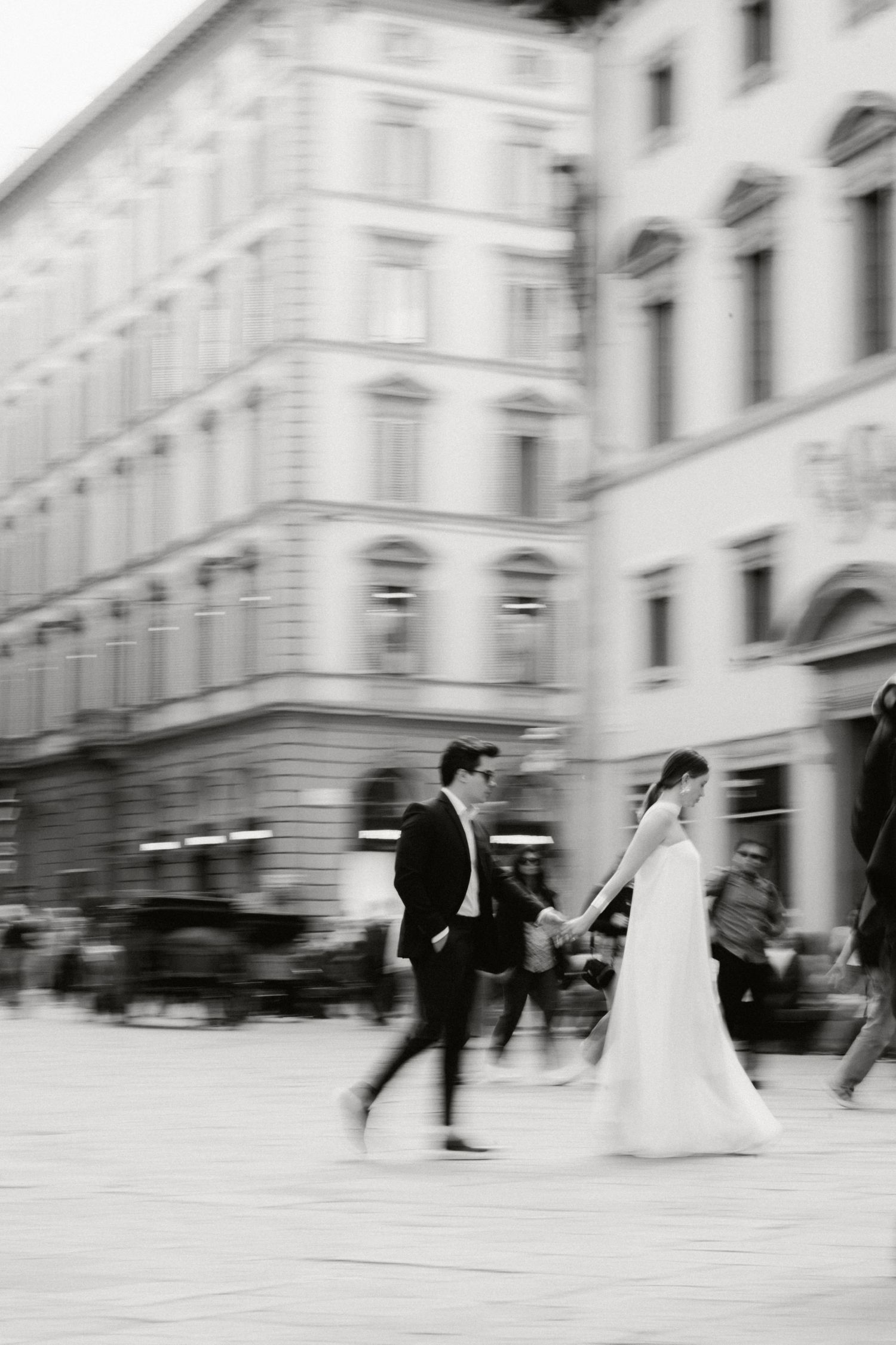 A wedding couple moves across a European city square in a sequence of motion blur black and white photographs.