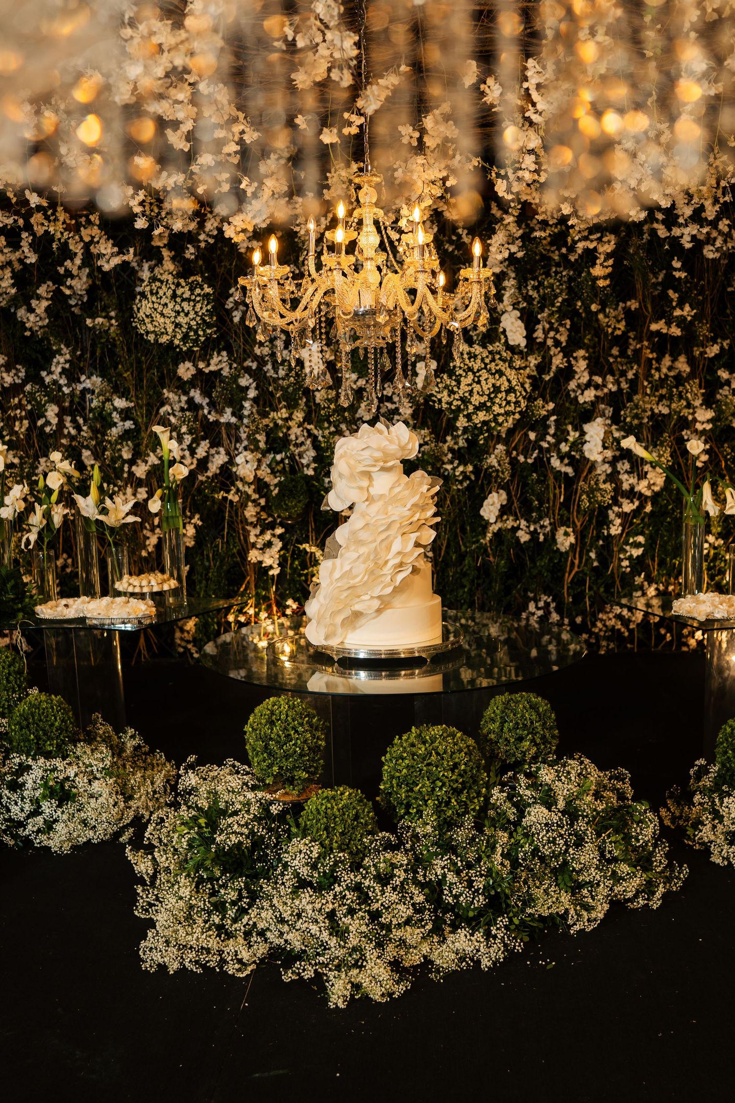 Elegant wedding cake display with crystal chandeliers and lush white floral arrangements creating a luxurious ambiance.