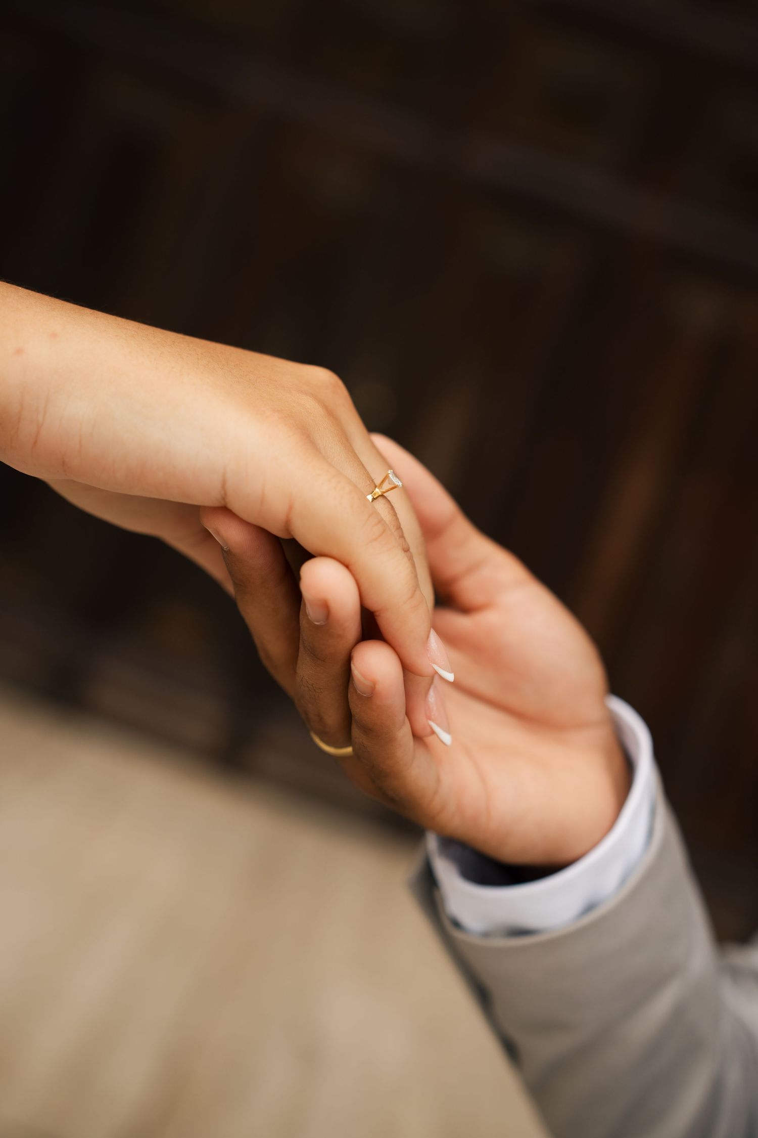 Close up of hands clasped together showing wedding rings against a neutral background.