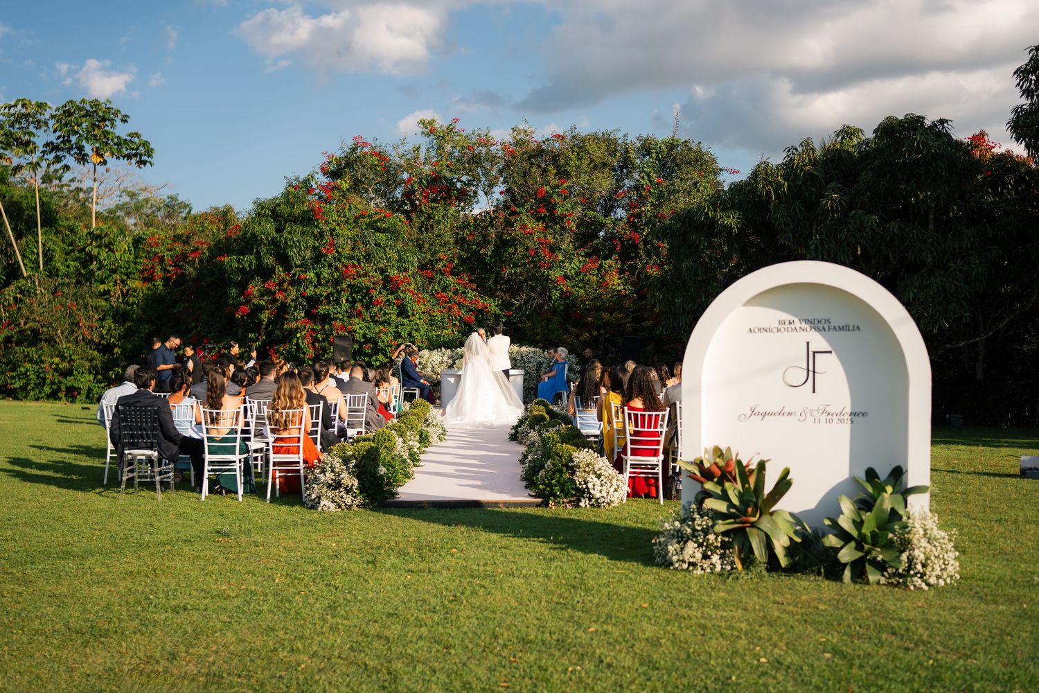 Red chairs arranged outdoors for a wedding ceremony with decorative elements in a garden setting.