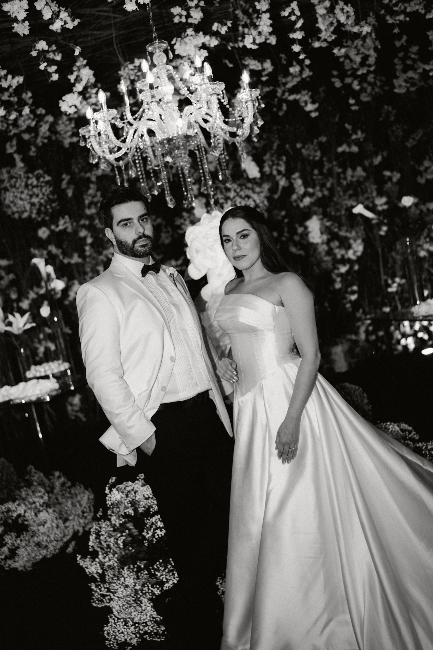 Black and white wedding photos showing a romantic couple in formal attire posing with white floral arrangements.