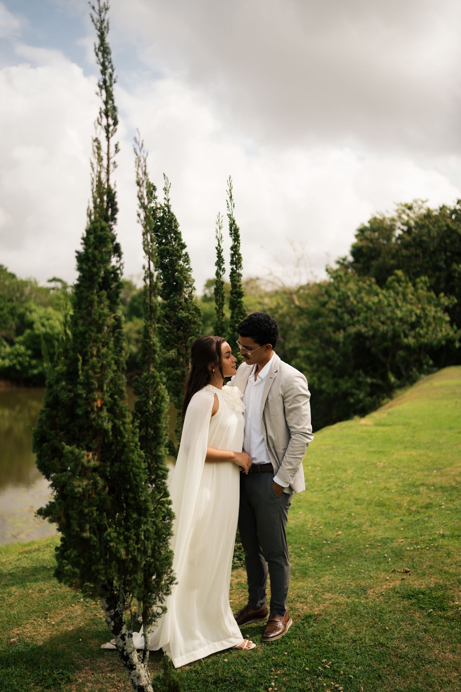 A romantic moment shared outdoors with tall cypress trees and cloudy skies in the background.