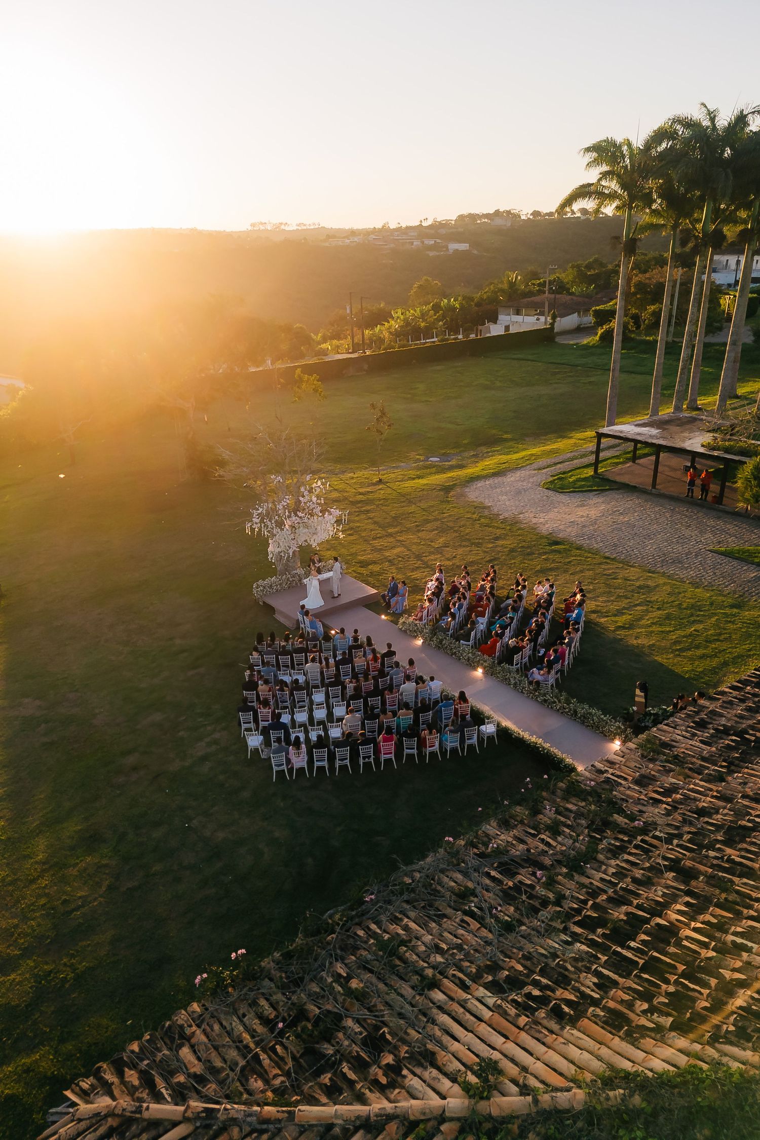 Aerial view of an outdoor wedding ceremony setup with chairs arranged on a hillside during golden hour.