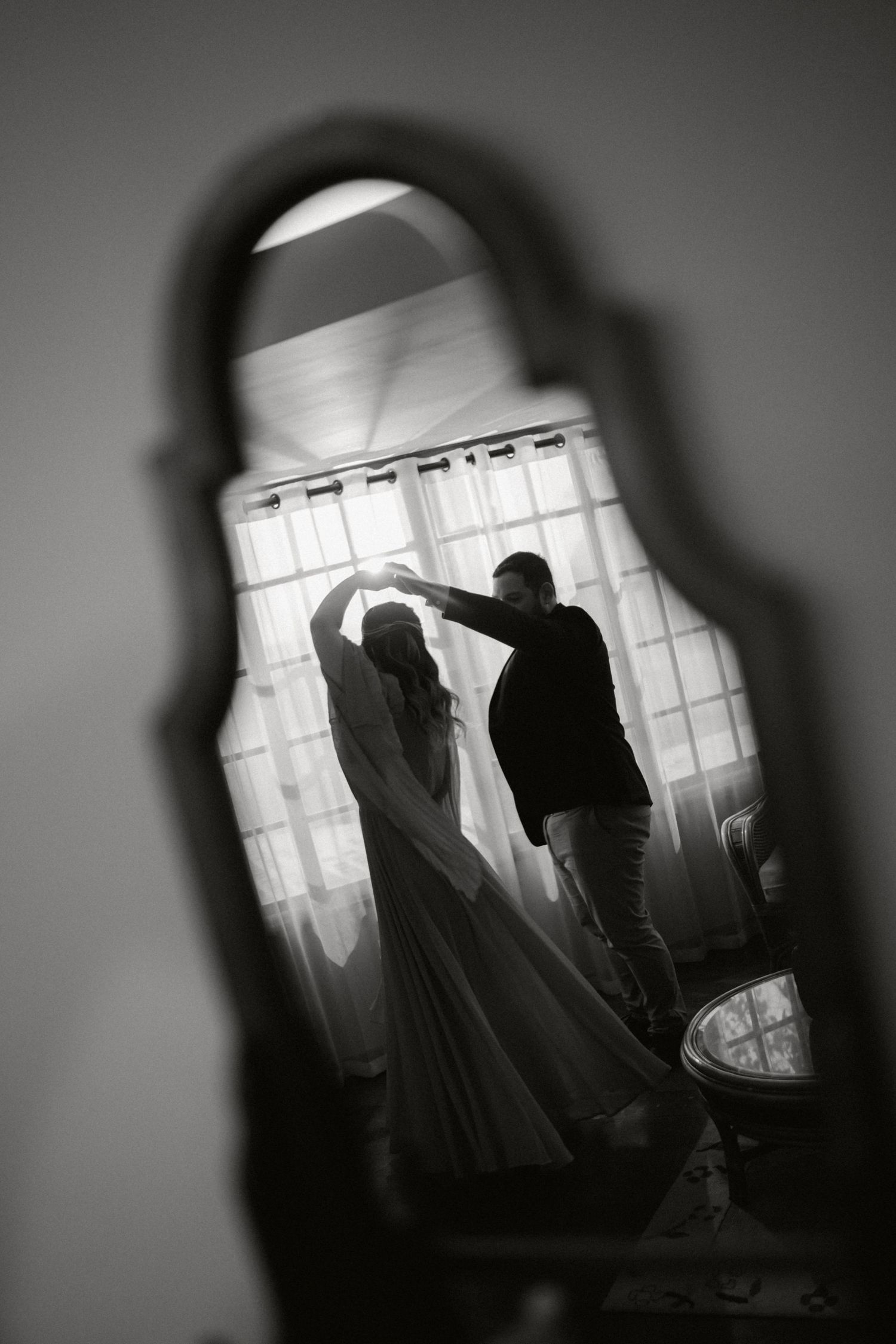 A silhouetted couple dancing in front of a window, viewed through a keyhole in dramatic black and white photography.