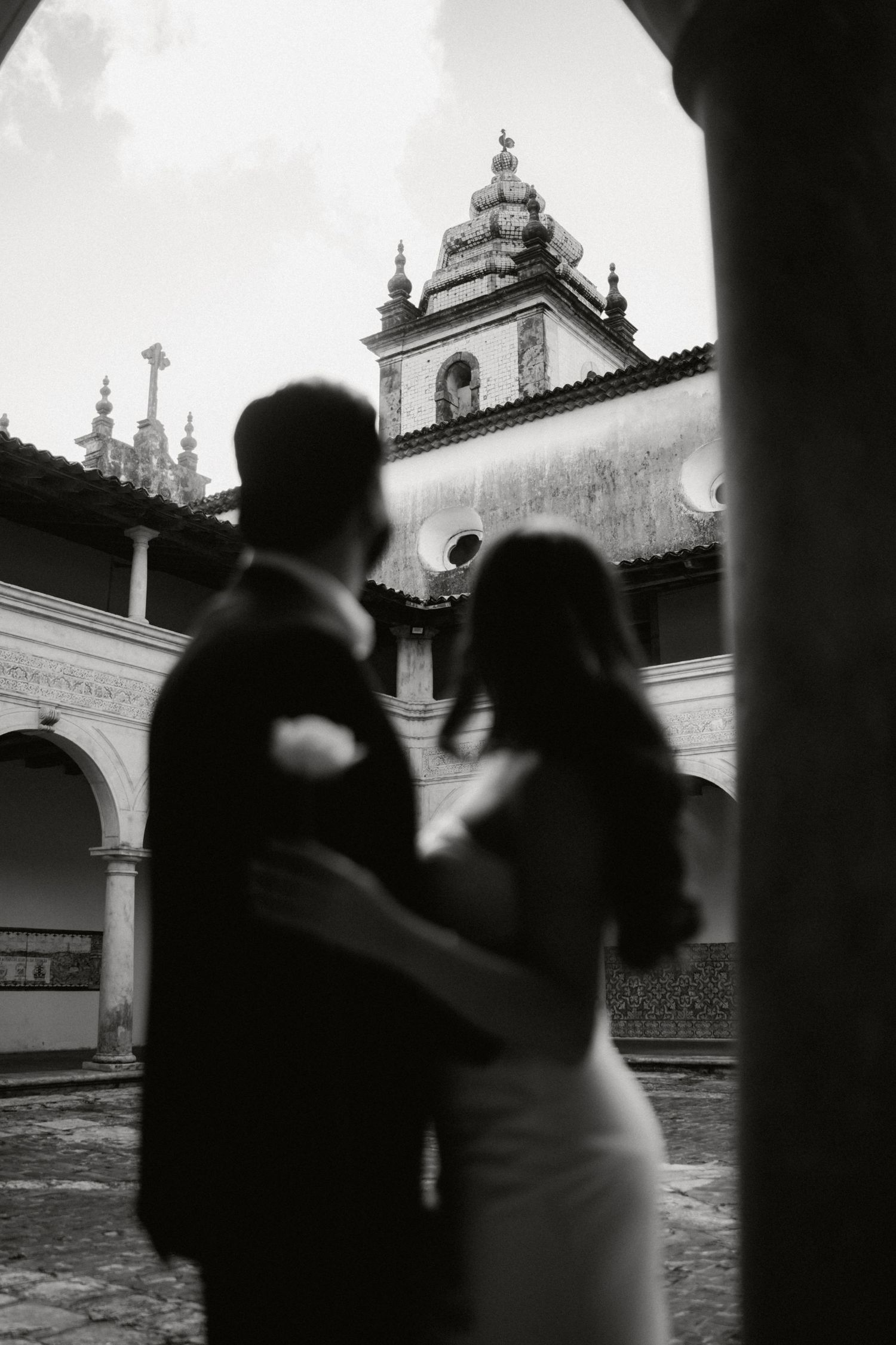 A black and white architectural photograph showing silhouettes against a church or monastery courtyard.
