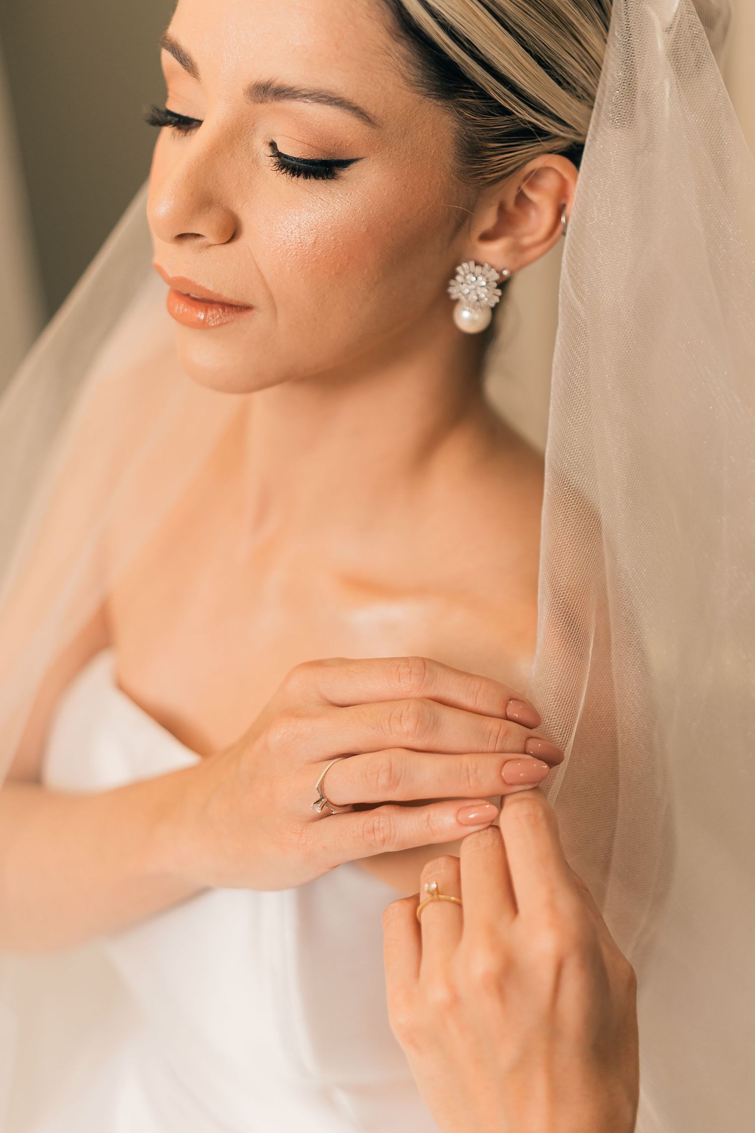 Close-up details of wedding jewelry and delicate hands against a soft neutral background.