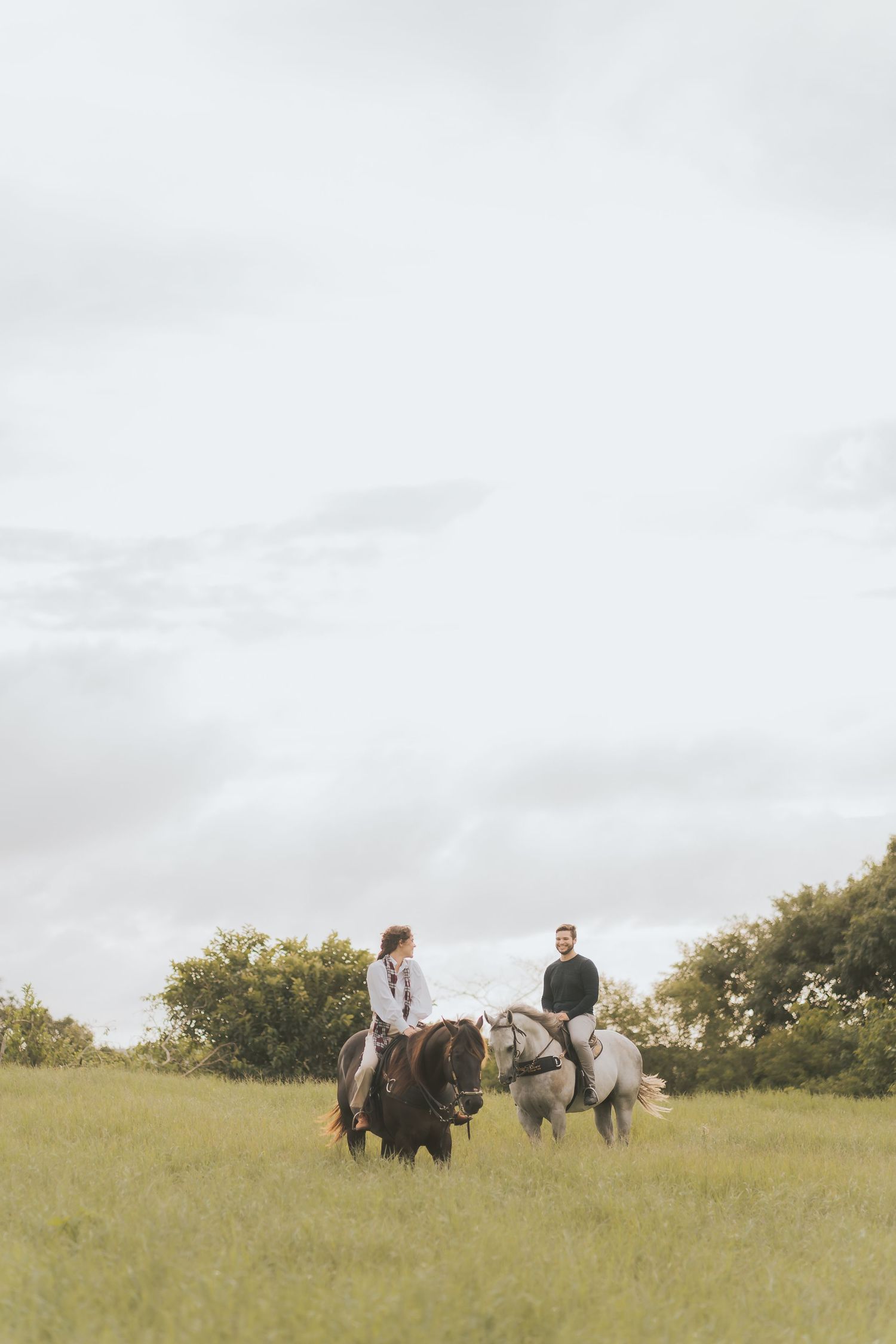 Couple walks with horses across a serene hilltop meadow on an overcast day.