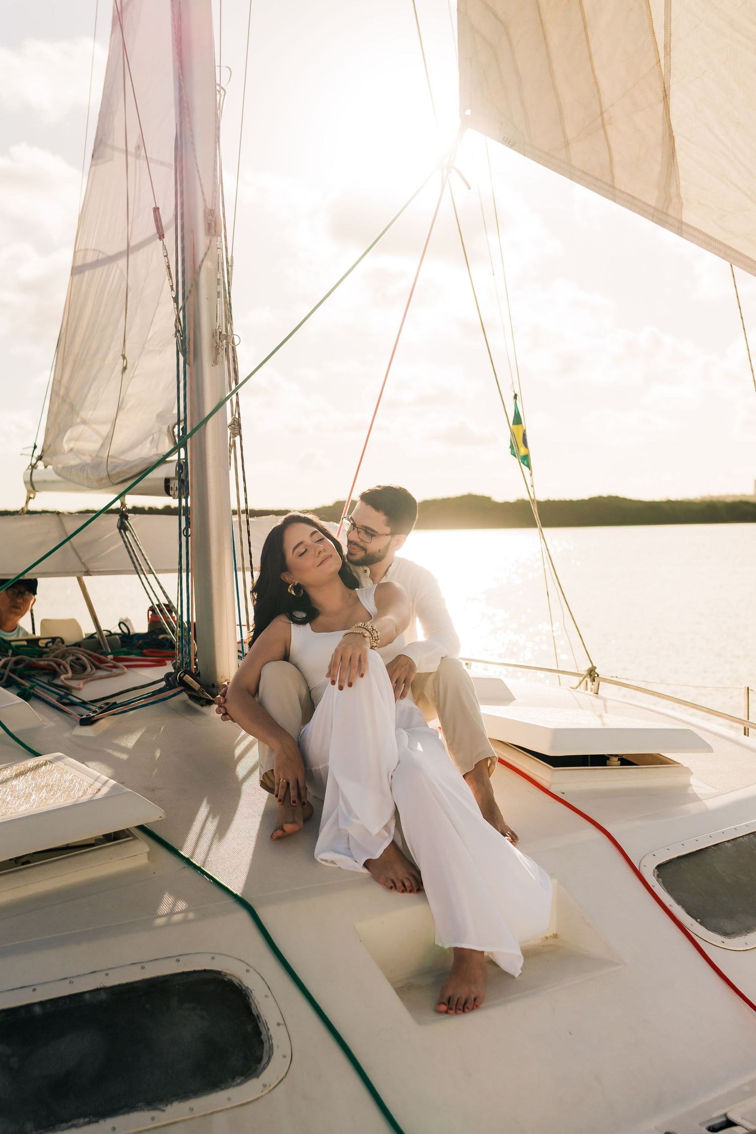 Couple in white clothing relaxes on a sailboat deck during a romantic sunset photoshoot.