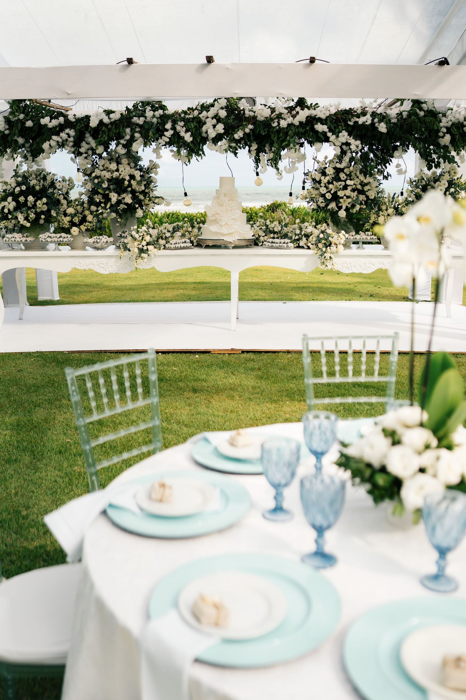 Outdoor wedding table setting with mint blue plates and white floral arrangements.