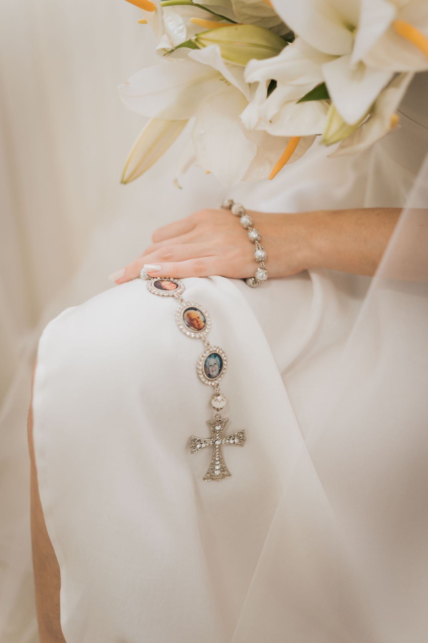 Close-up of delicate white beaded rosary with cross pendant against white fabric background.