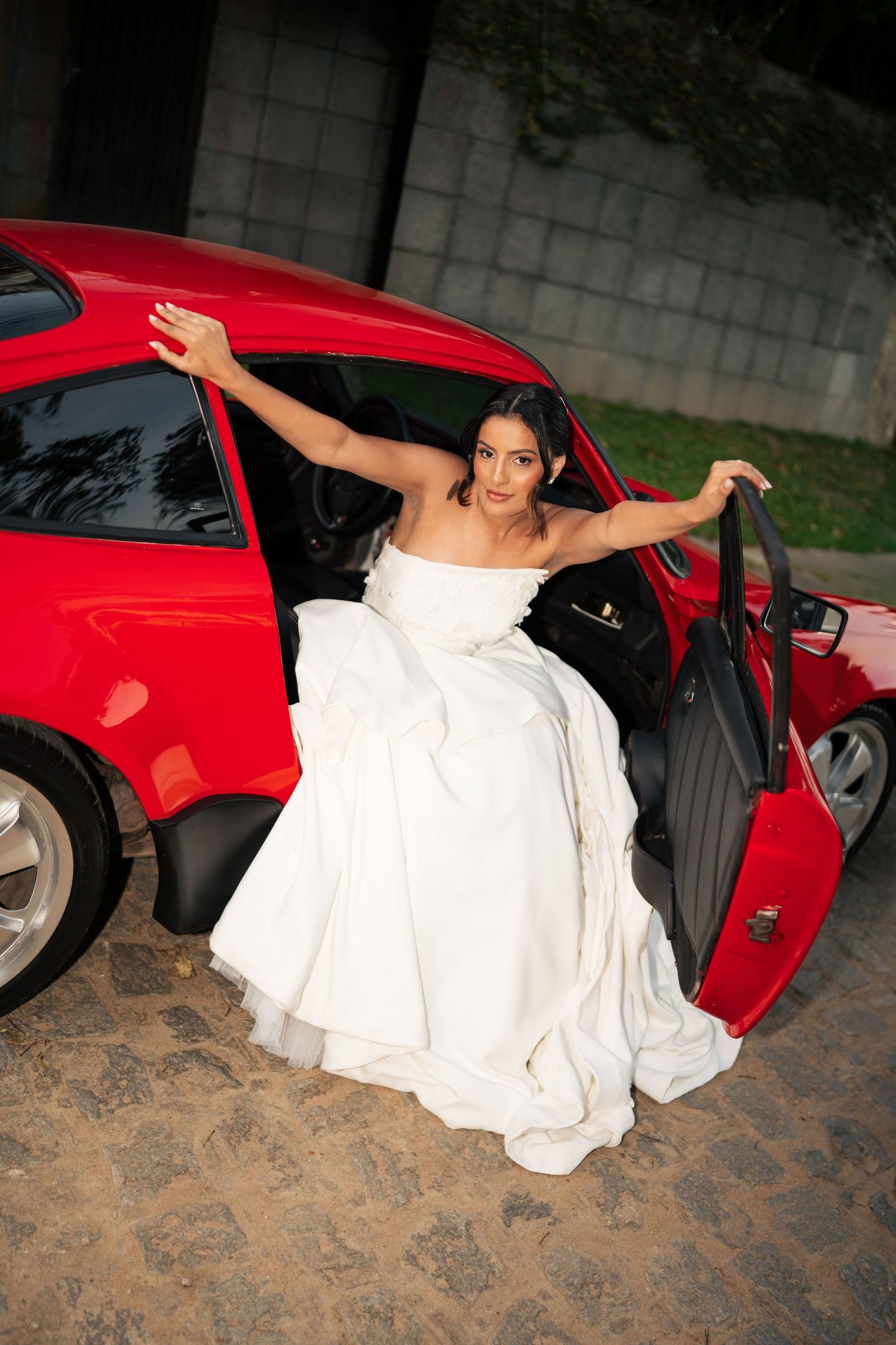A sequence showing someone in a white dress getting into a bright red sports car on a brick driveway.