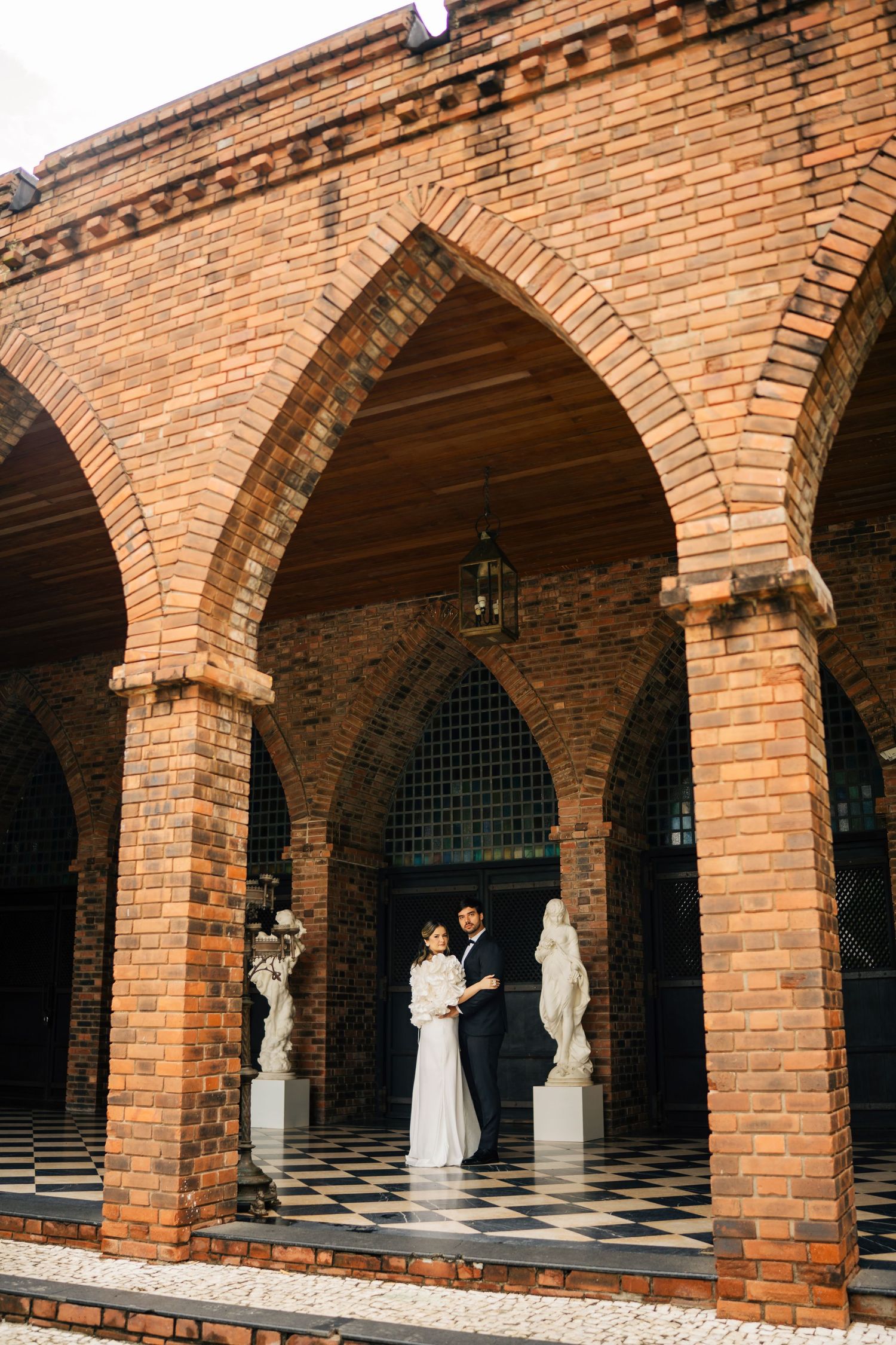 A series of brick archways with white statues displayed underneath in a classical colonnade.