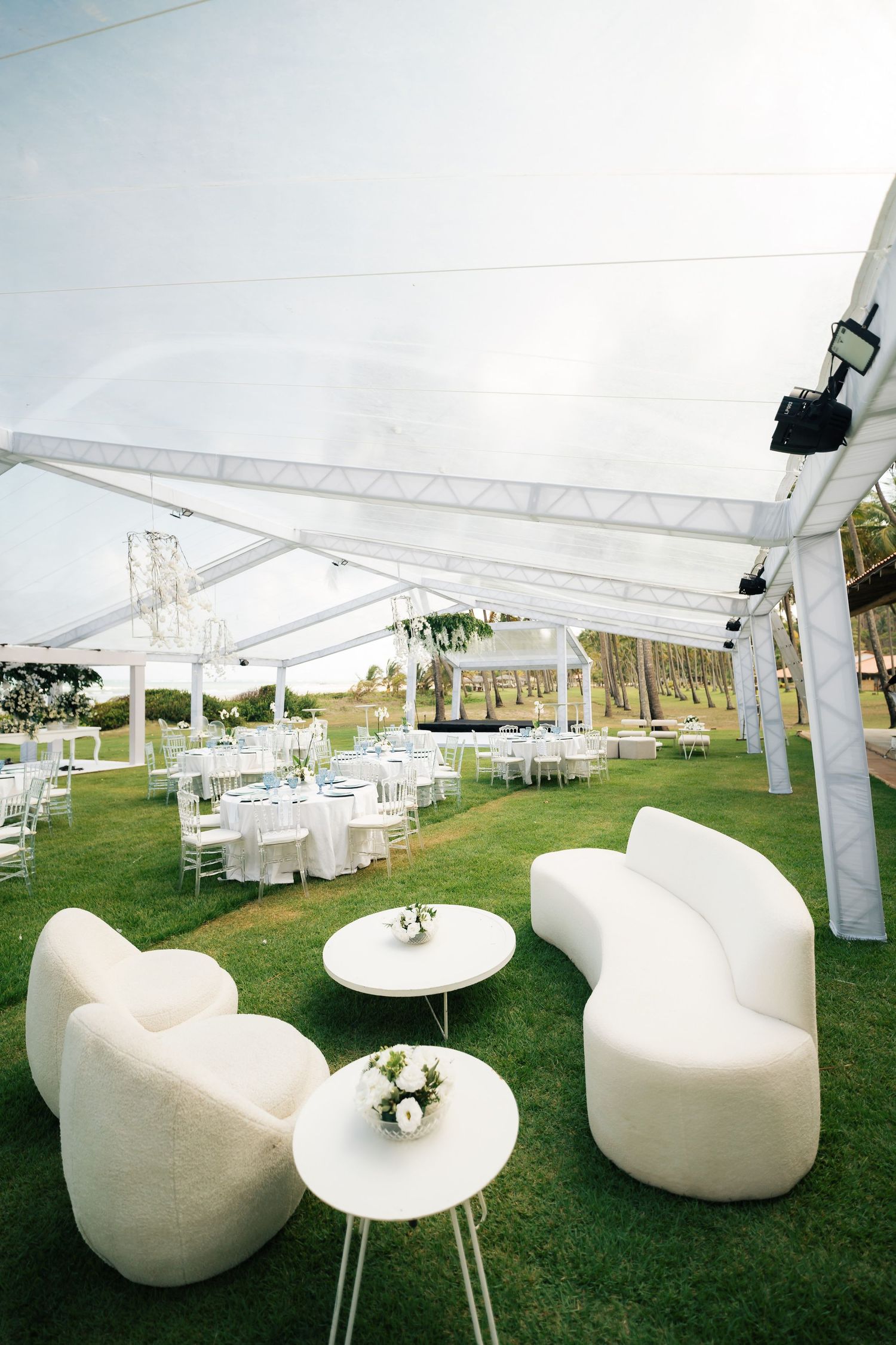 Modern white lounge furniture setup under outdoor tent canopy on grass lawn.