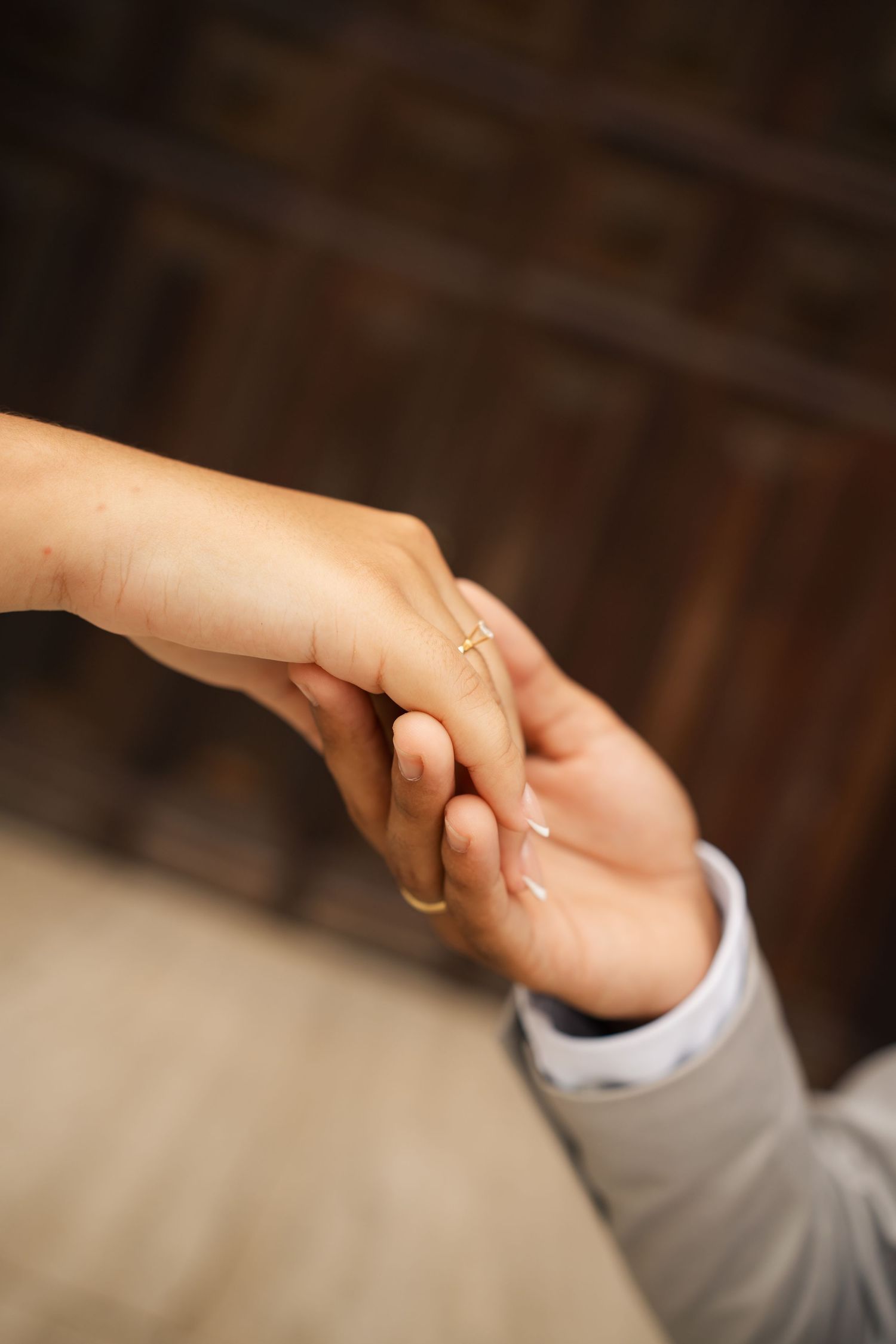 Two hands gently clasp together in a tender moment against a dark wooden background.