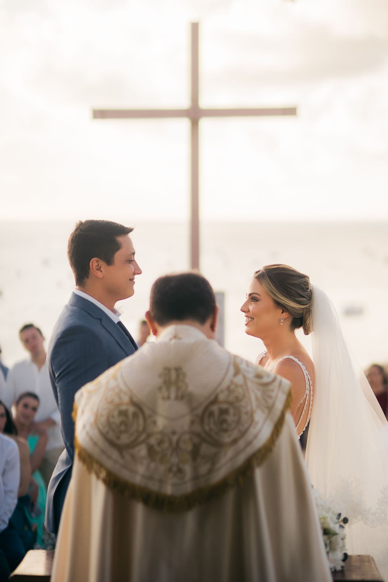Couple stands before a priest during a traditional wedding ceremony in a bright church setting.