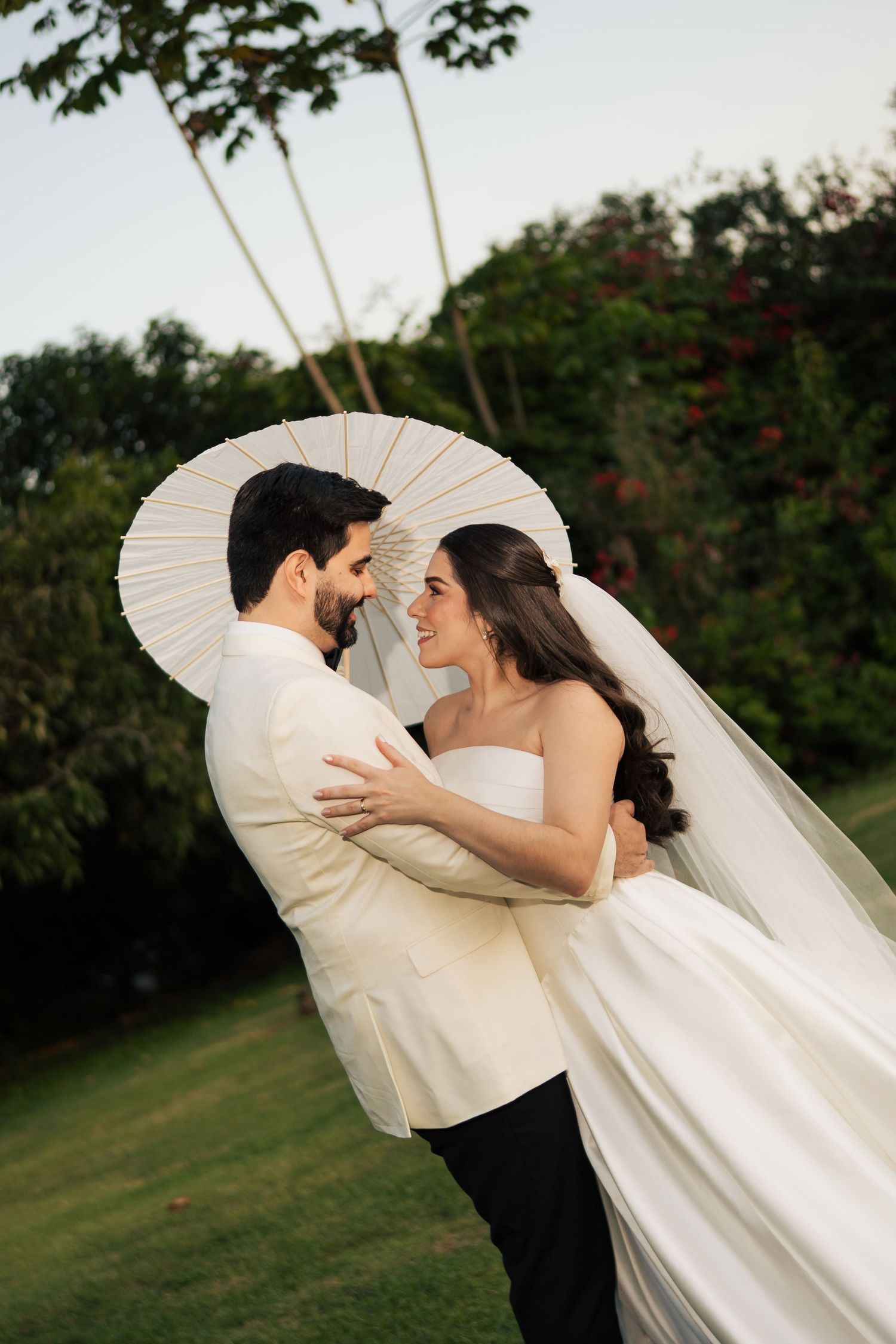 Romantic wedding portrait with couple holding a white parasol in a garden setting.