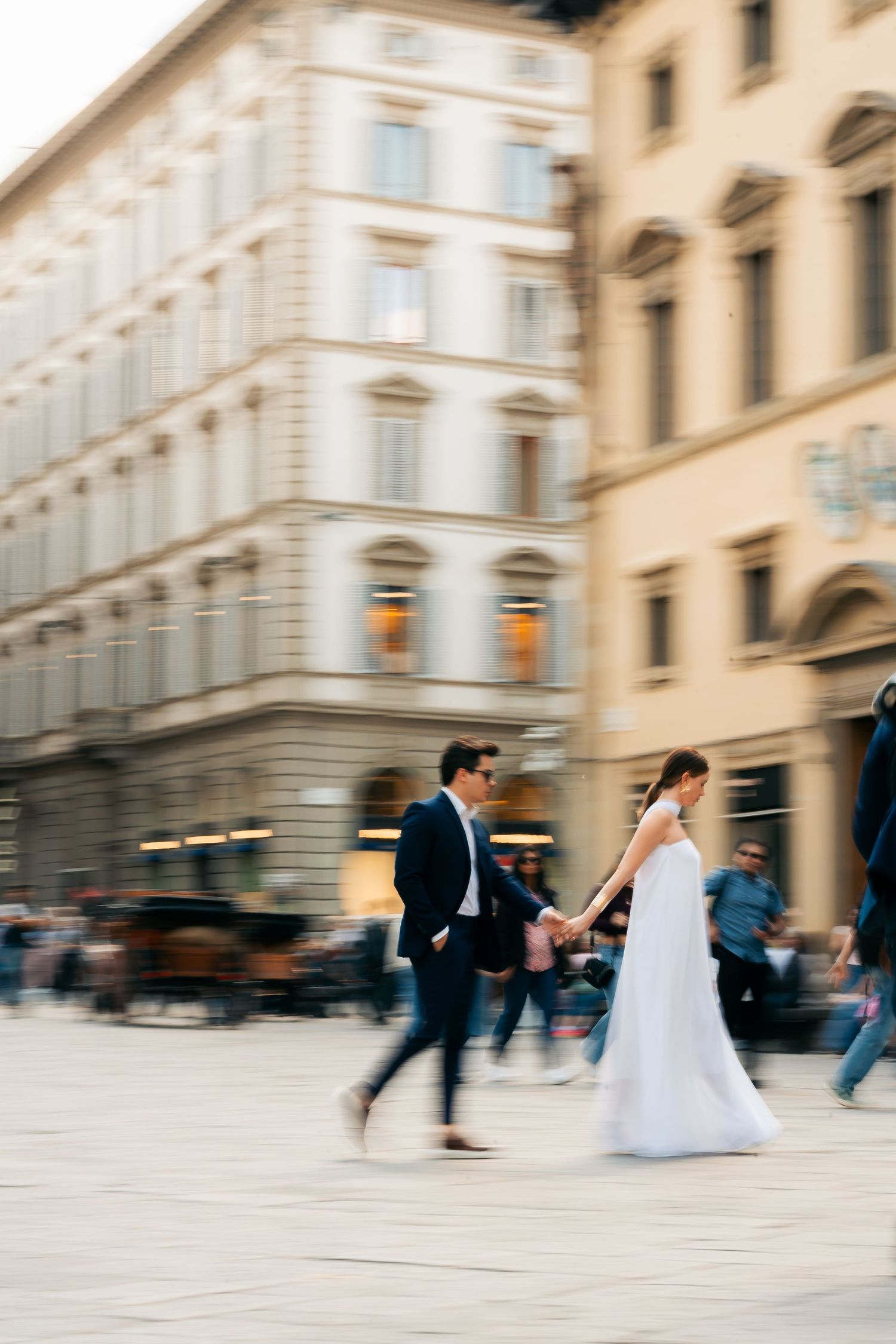 Motion-blurred couple in wedding attire walking through historic European city street with classic architecture.