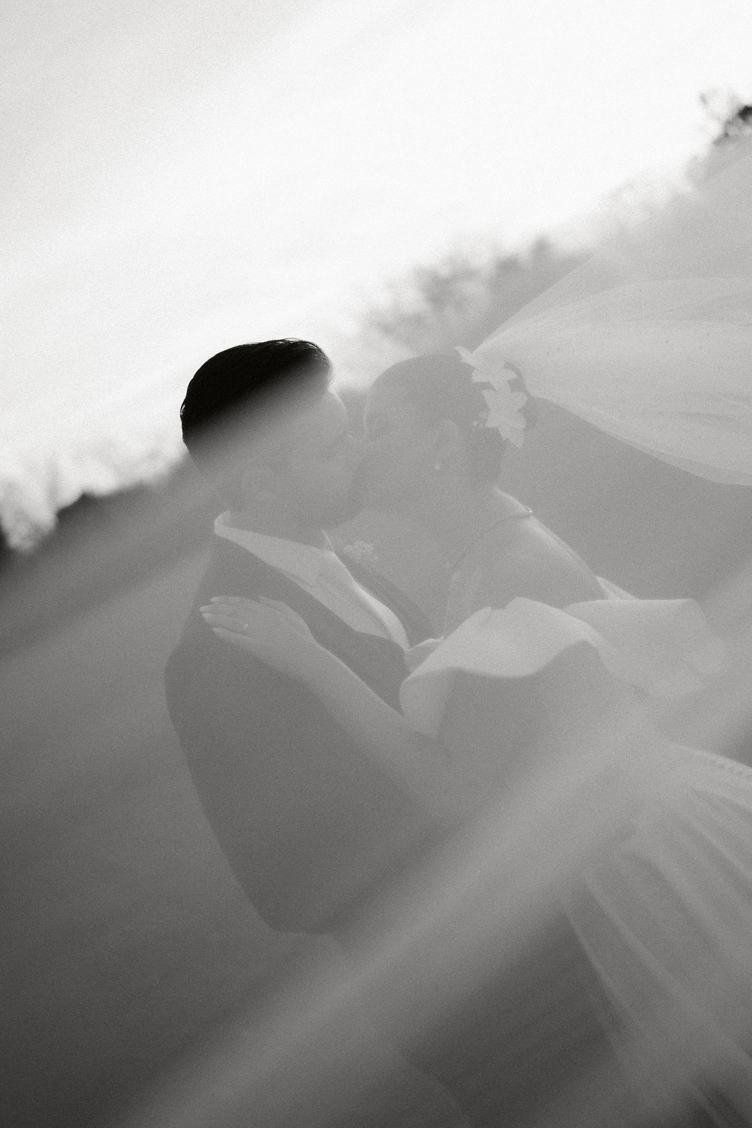 Artistic black and white photo of a bride with flowing veil in soft focus.
