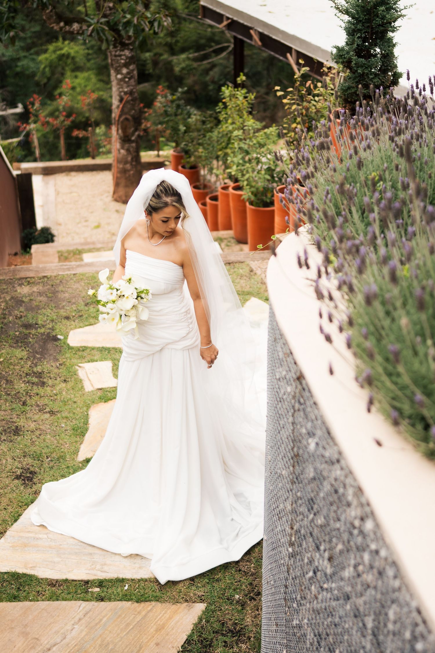 A flowing white wedding dress twirls gracefully against a backdrop of lavender flowers in a garden setting.