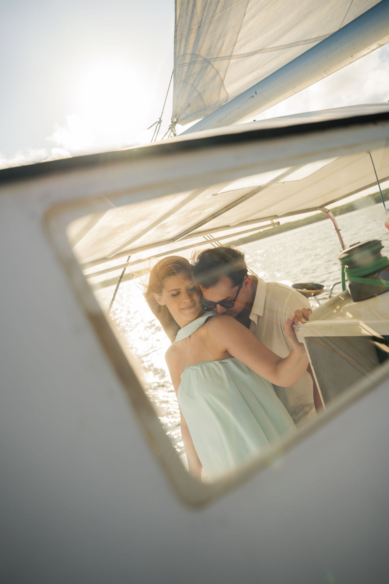 A couple embraces intimately under white sailboat canvas in soft natural lighting.