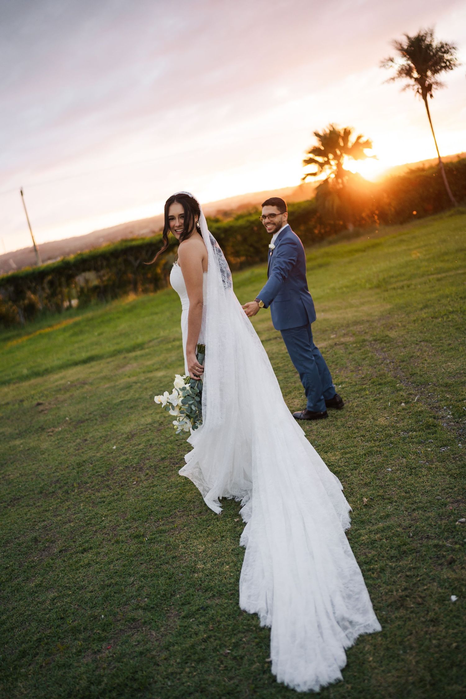 A wedding couple poses at sunset with palm trees and mountains in the background.
