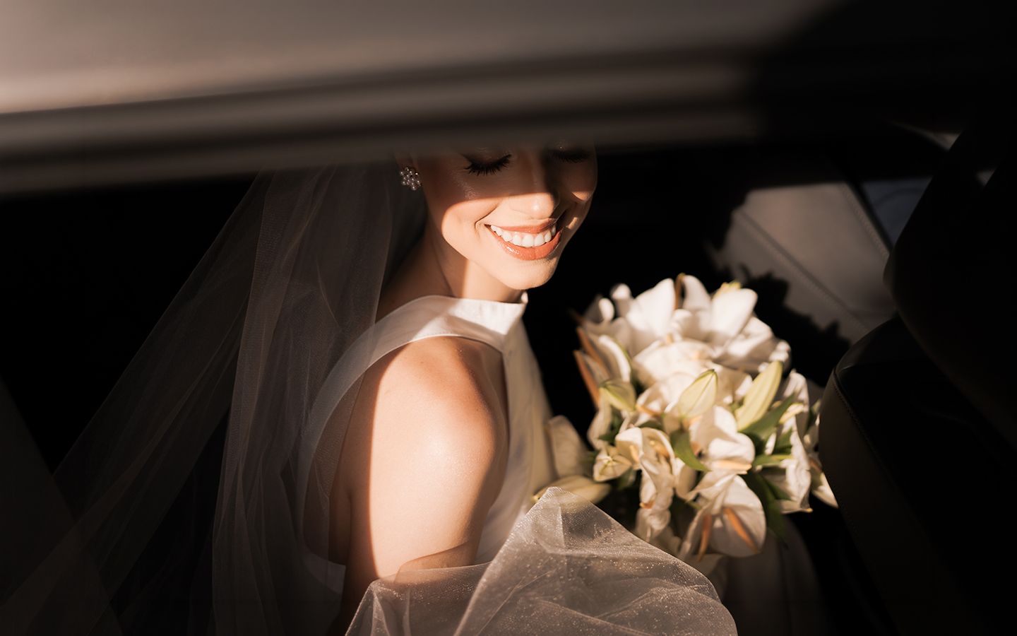 A wedding scene showing a glimpse of a bride in a car holding an elegant white bouquet.