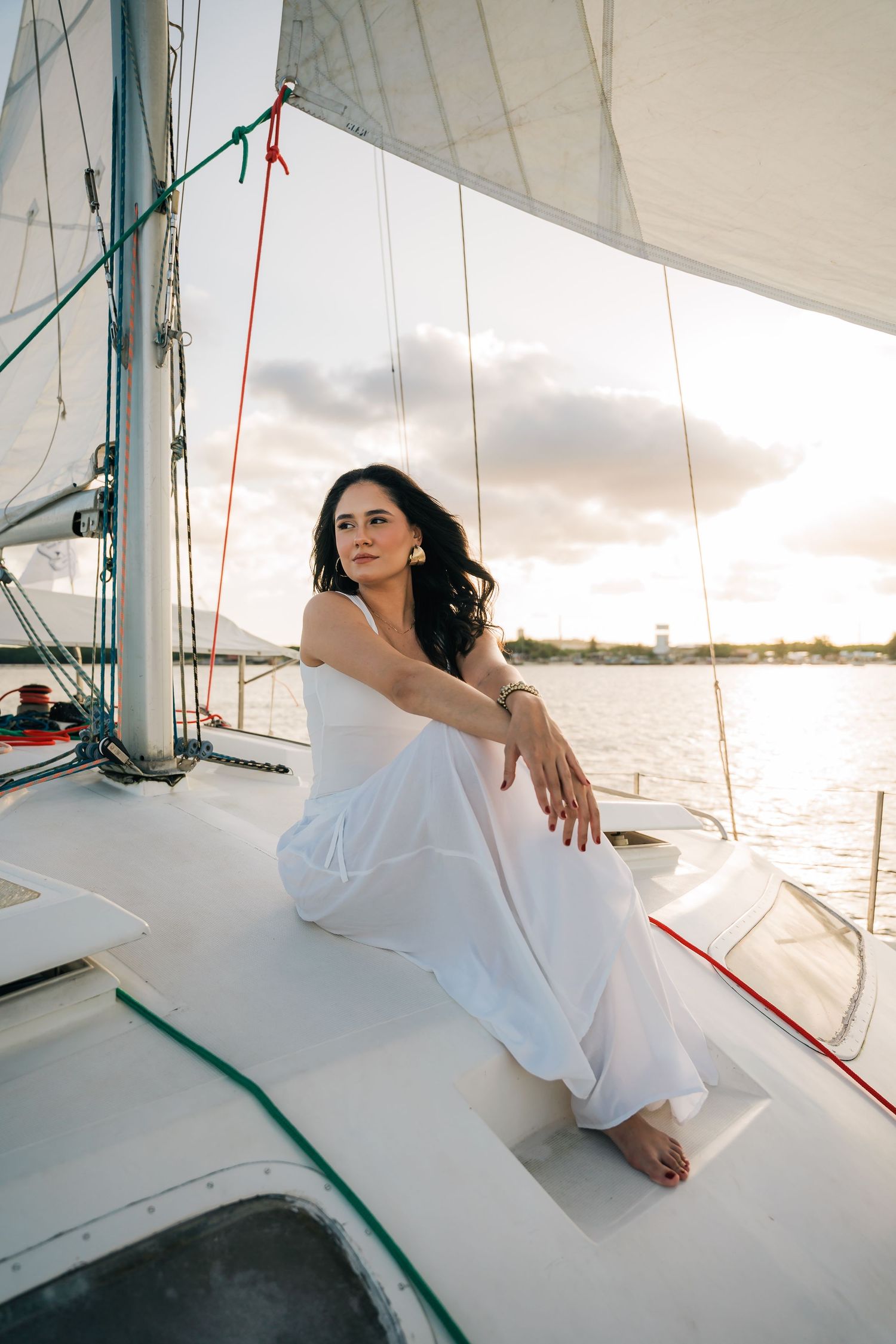 A series of photos showing someone in a white dress lounging on a sailboat deck during sunset.