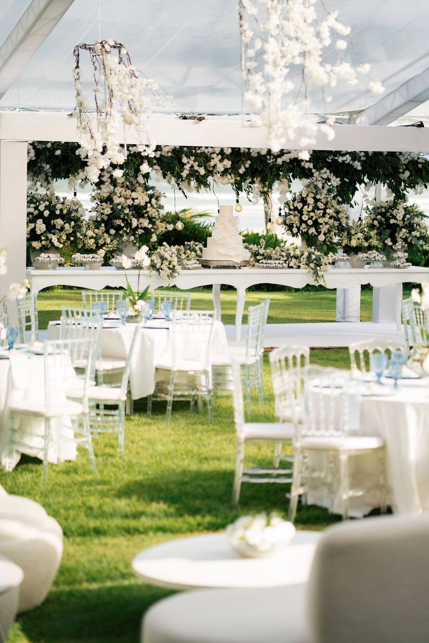 Outdoor wedding reception setup with white chairs and twinkling lights under a white pergola.