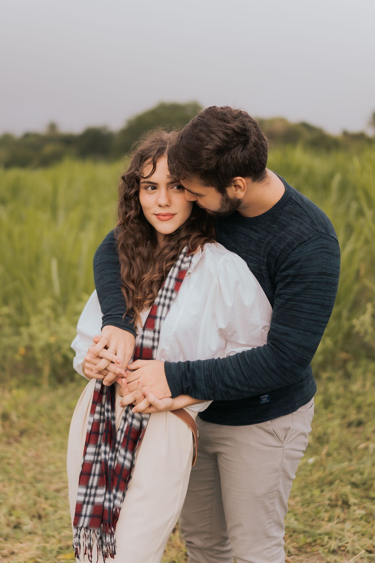 A couple embraces in a romantic moment while standing in a sunlit field on a warm afternoon.