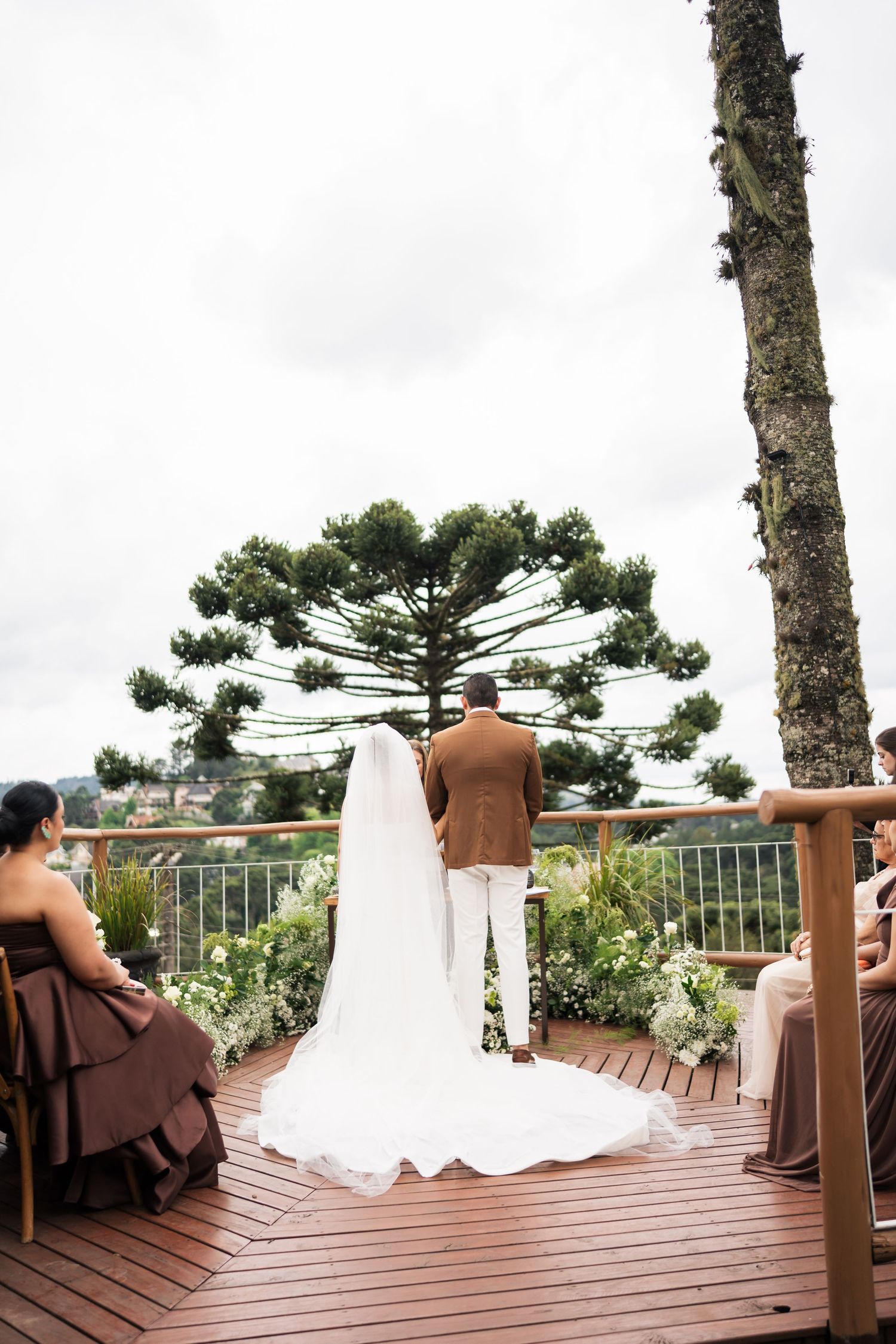 Wedding couple standing on a wooden deck overlooking a scenic view with large araucaria trees.