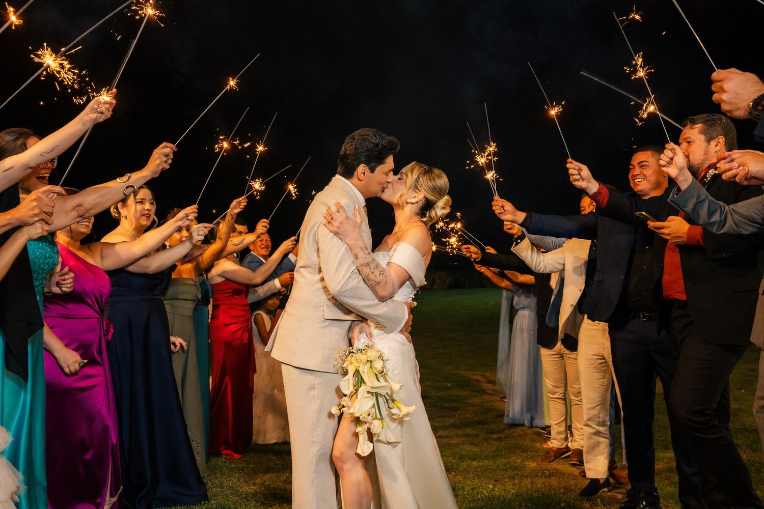 Wedding guests hold sparklers creating magical light trails during an outdoor evening celebration.