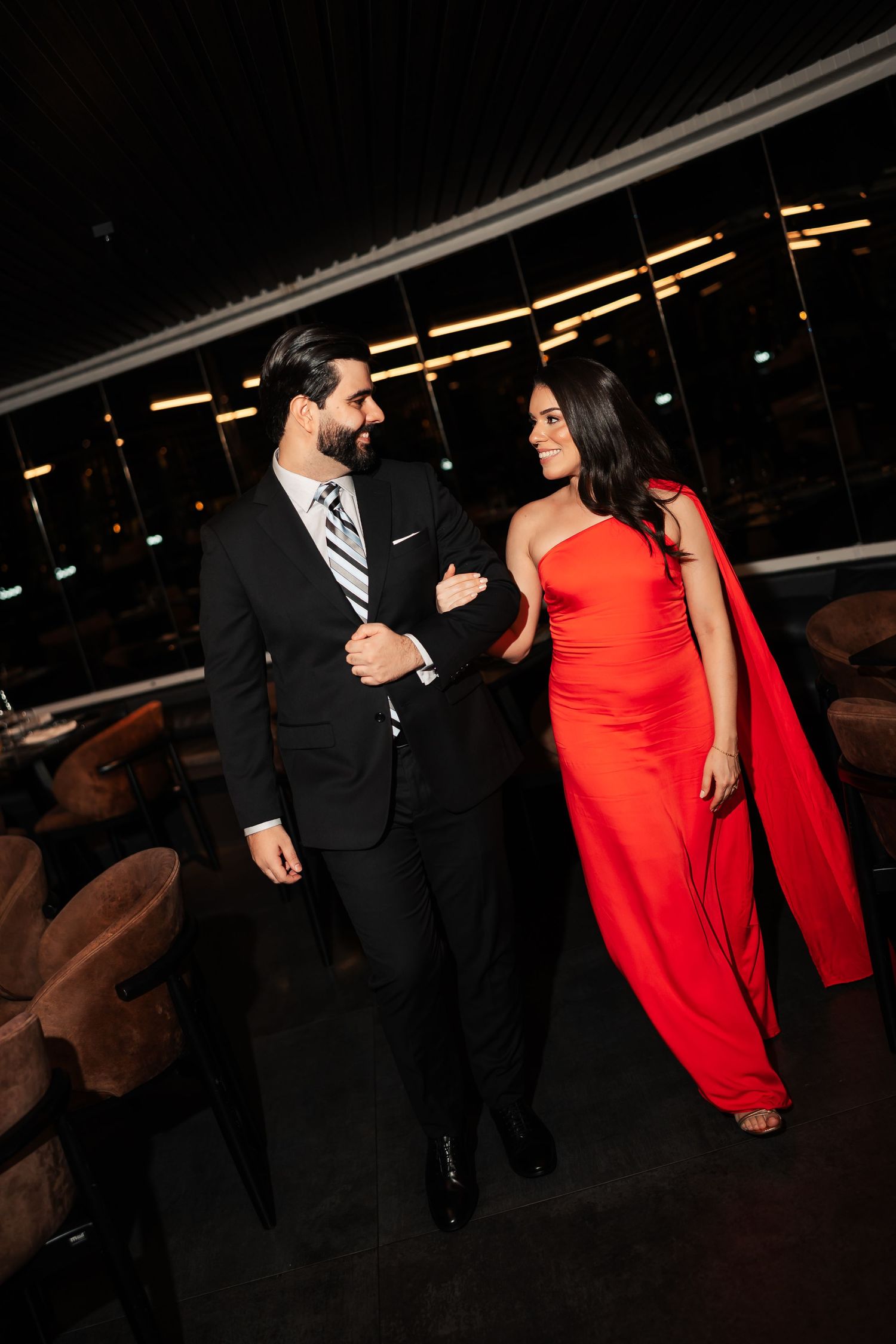 A couple in formal attire, with a woman in a vibrant red dress and man in black suit, dancing at an evening event.