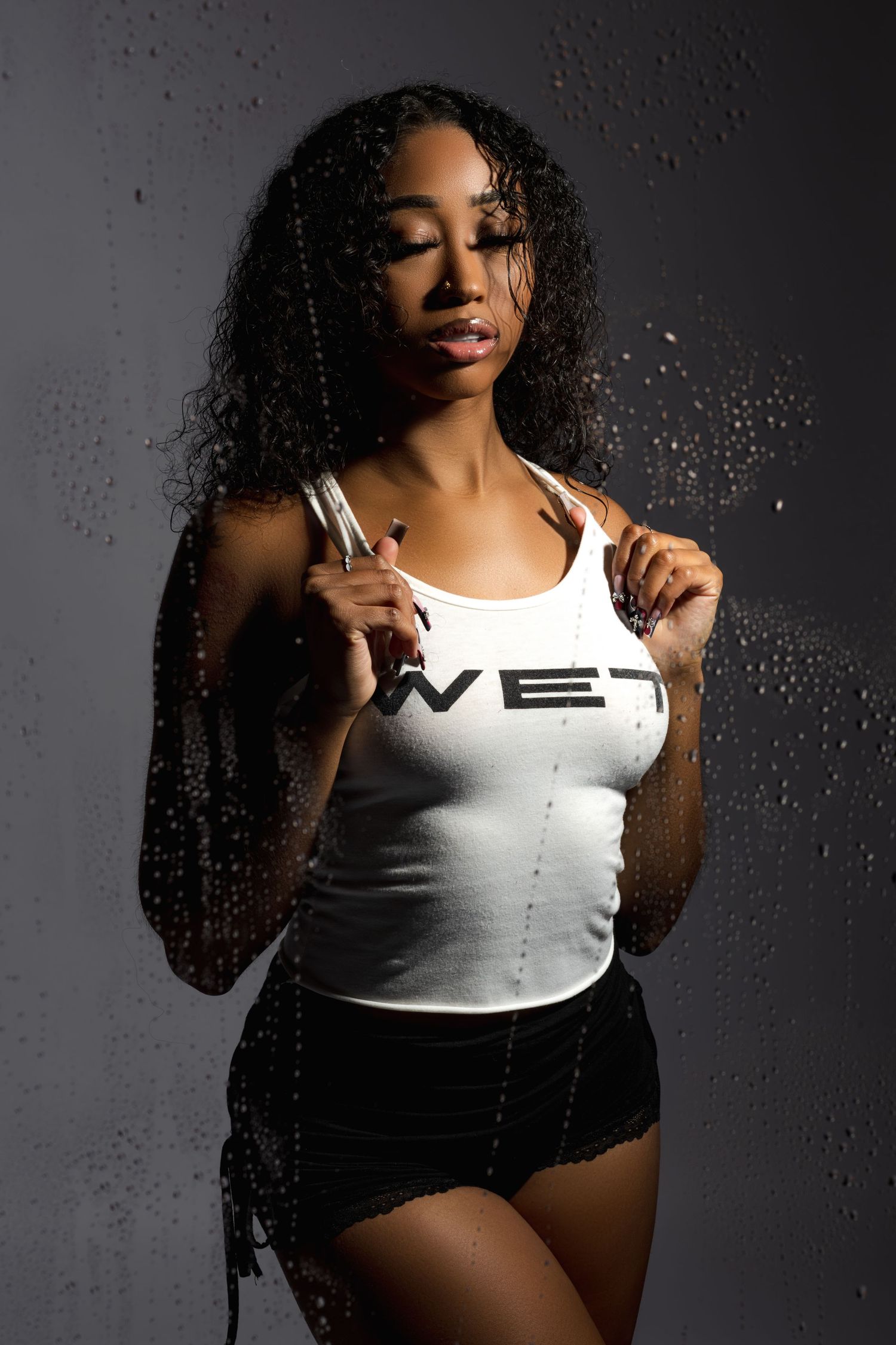 Portrait of woman in white tank top against dark background with water droplets.