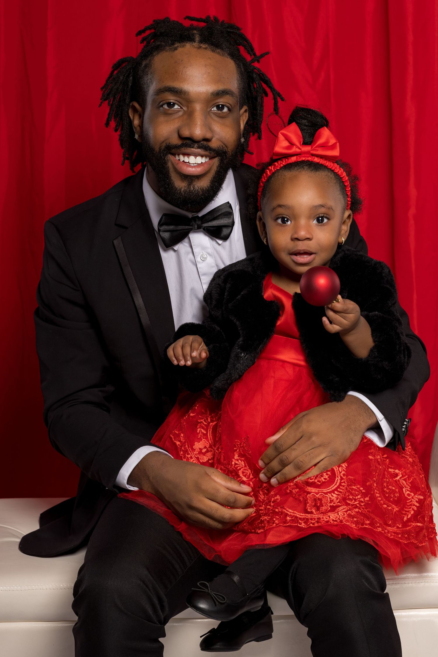 A parent and child pose together in formal attire against a red backdrop for an elegant portrait.