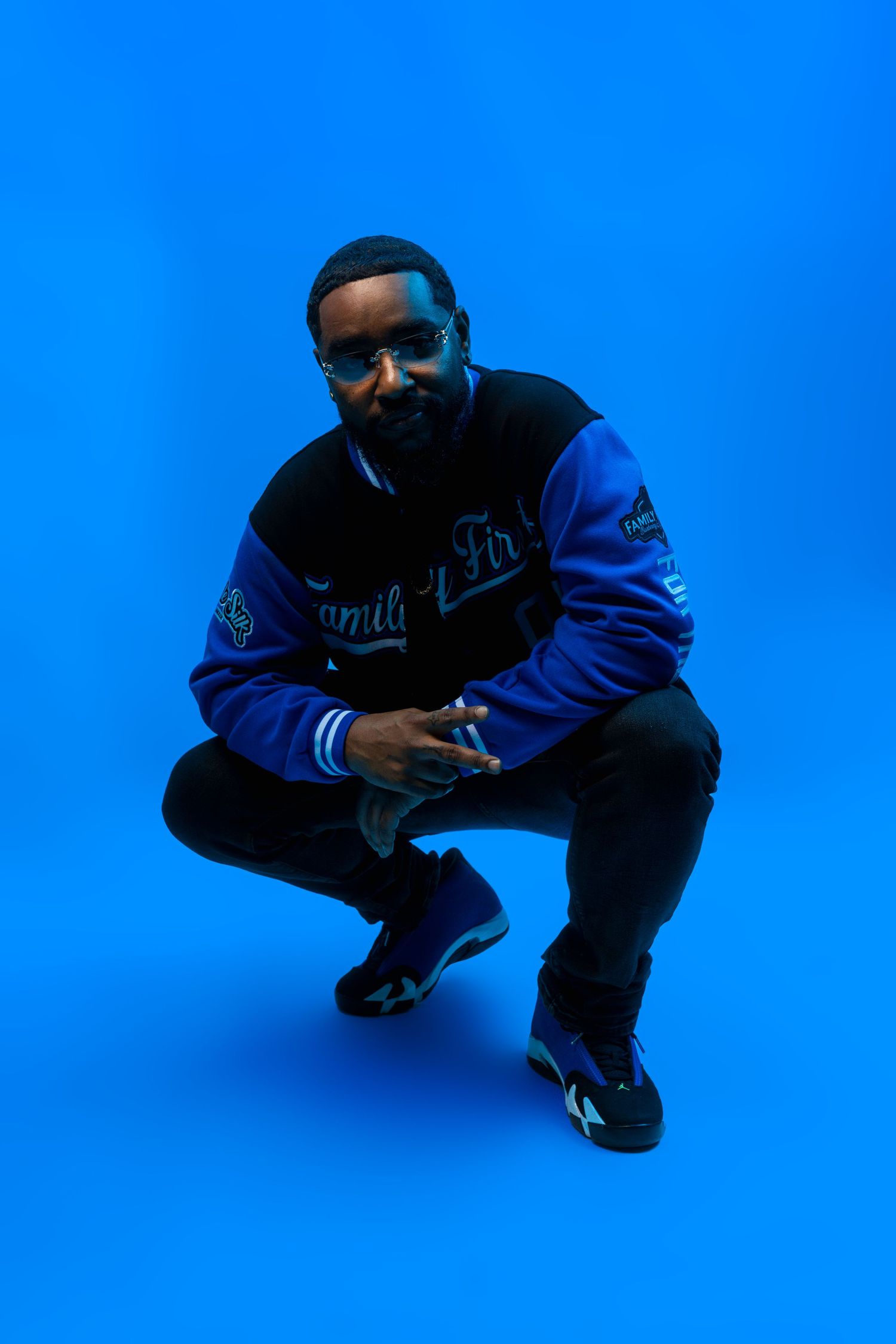 Person in blue and black varsity jacket crouching against bright blue background.