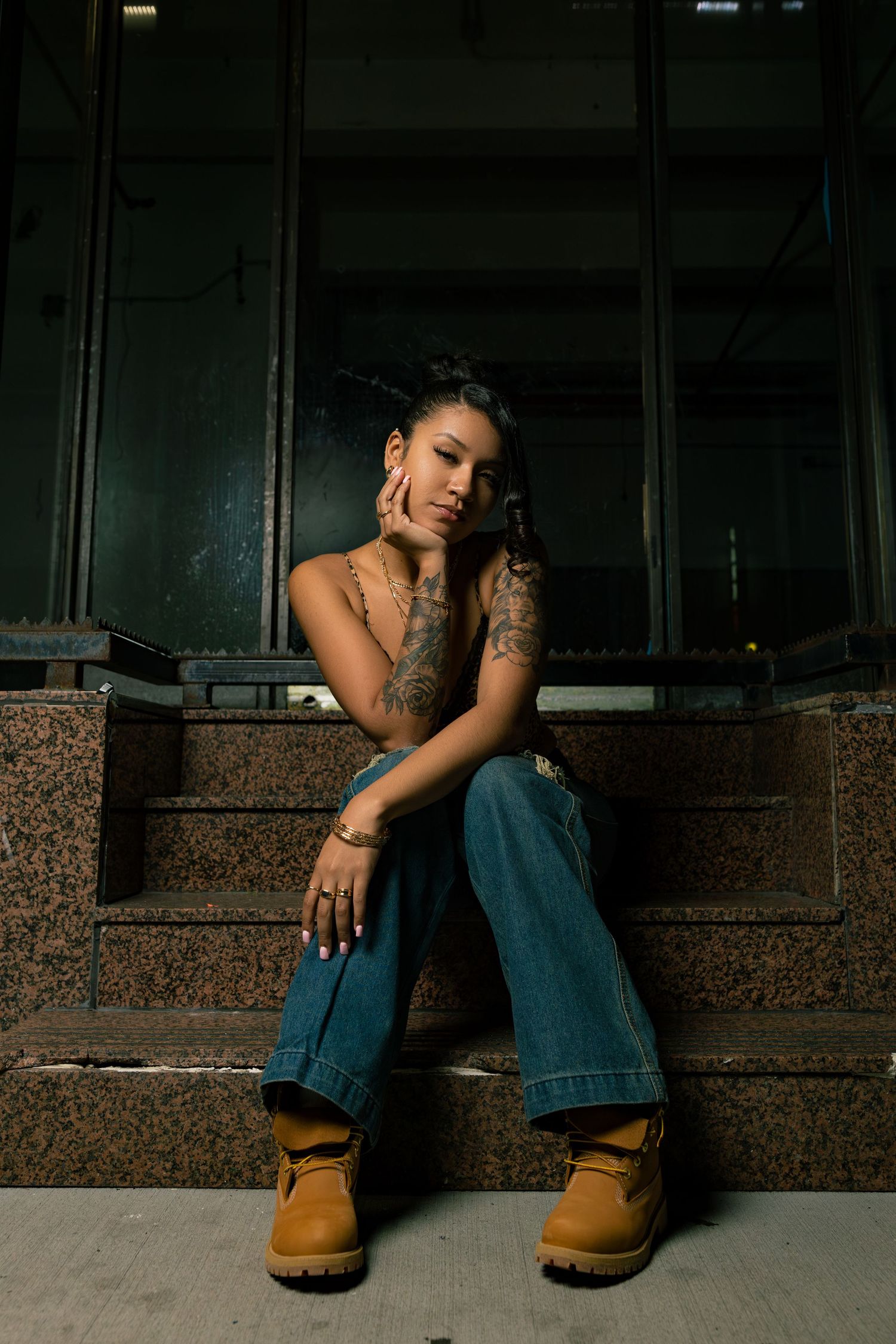 Moody portrait of person in casual wear and work boots sitting against dark urban wall.