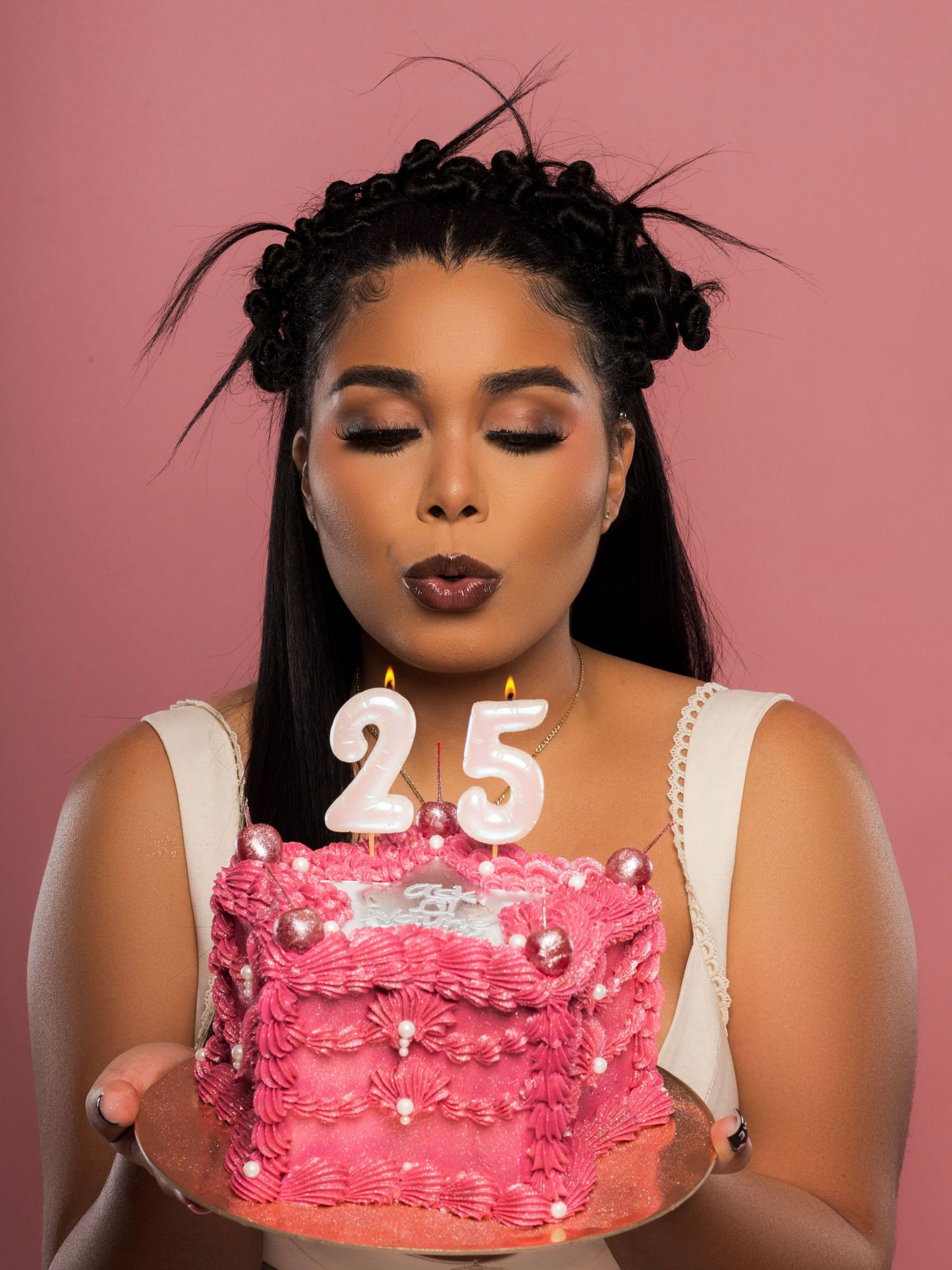 A pink birthday cake with white decorative details and the number 25 on top being displayed in a photo series.