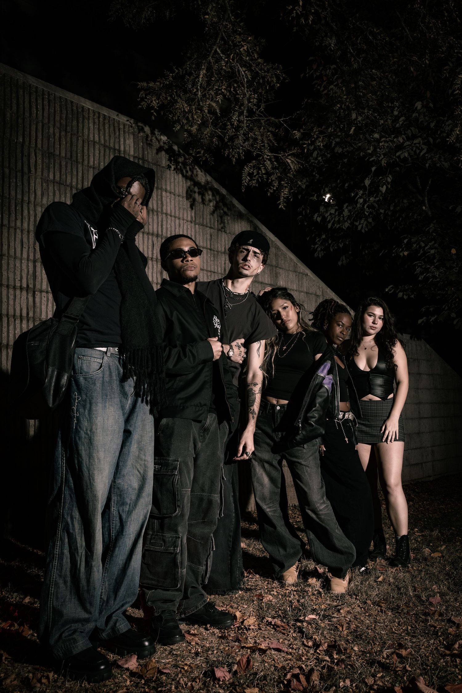 A group of people in dark clothing pose dramatically at night in a sequence of artistic performance shots.